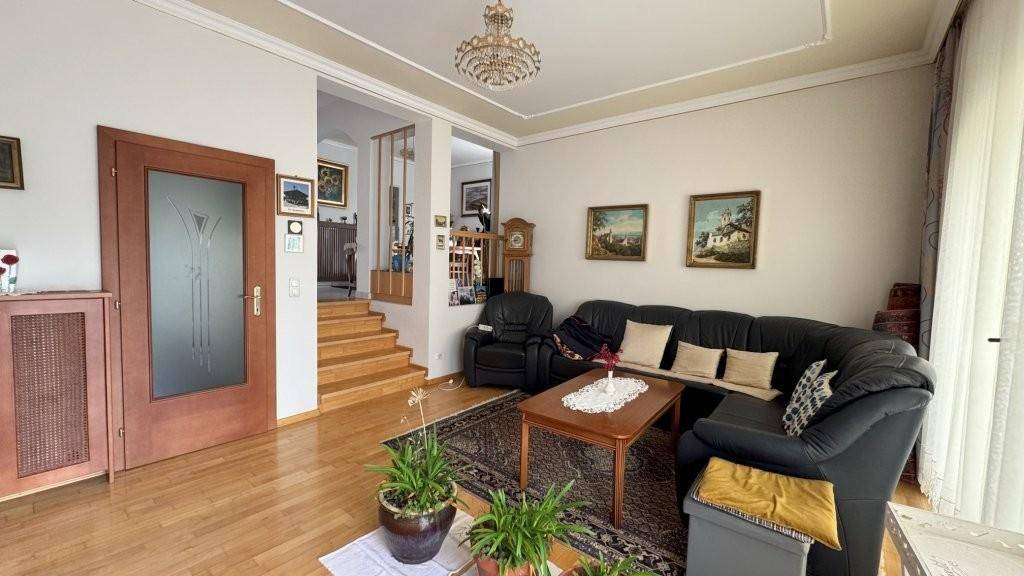 Helles Wohnzimmer mit Ledersofa, Holzboden und Zugang zu einer Treppe, klassisch eingerichtet.