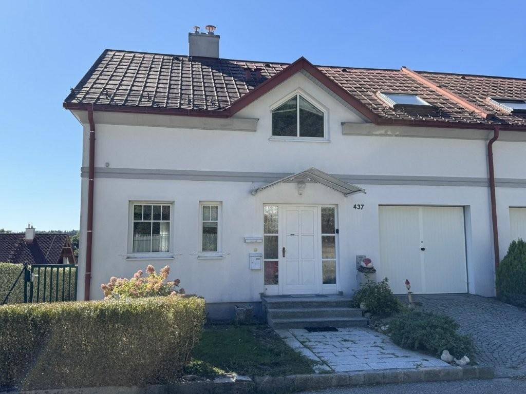 Vorderansicht des Reihenhauses mit Eingangsbereich, Garage und gepflegtem Vorgarten unter klarem Himmel.