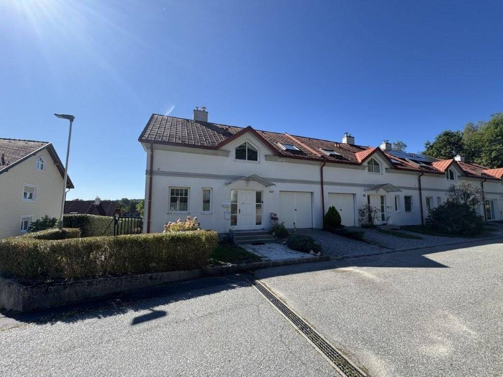 Reihenhäuser in einer ruhigen Wohngegend mit gepflegten Vorgärten und Garagen unter blauem Himmel.
