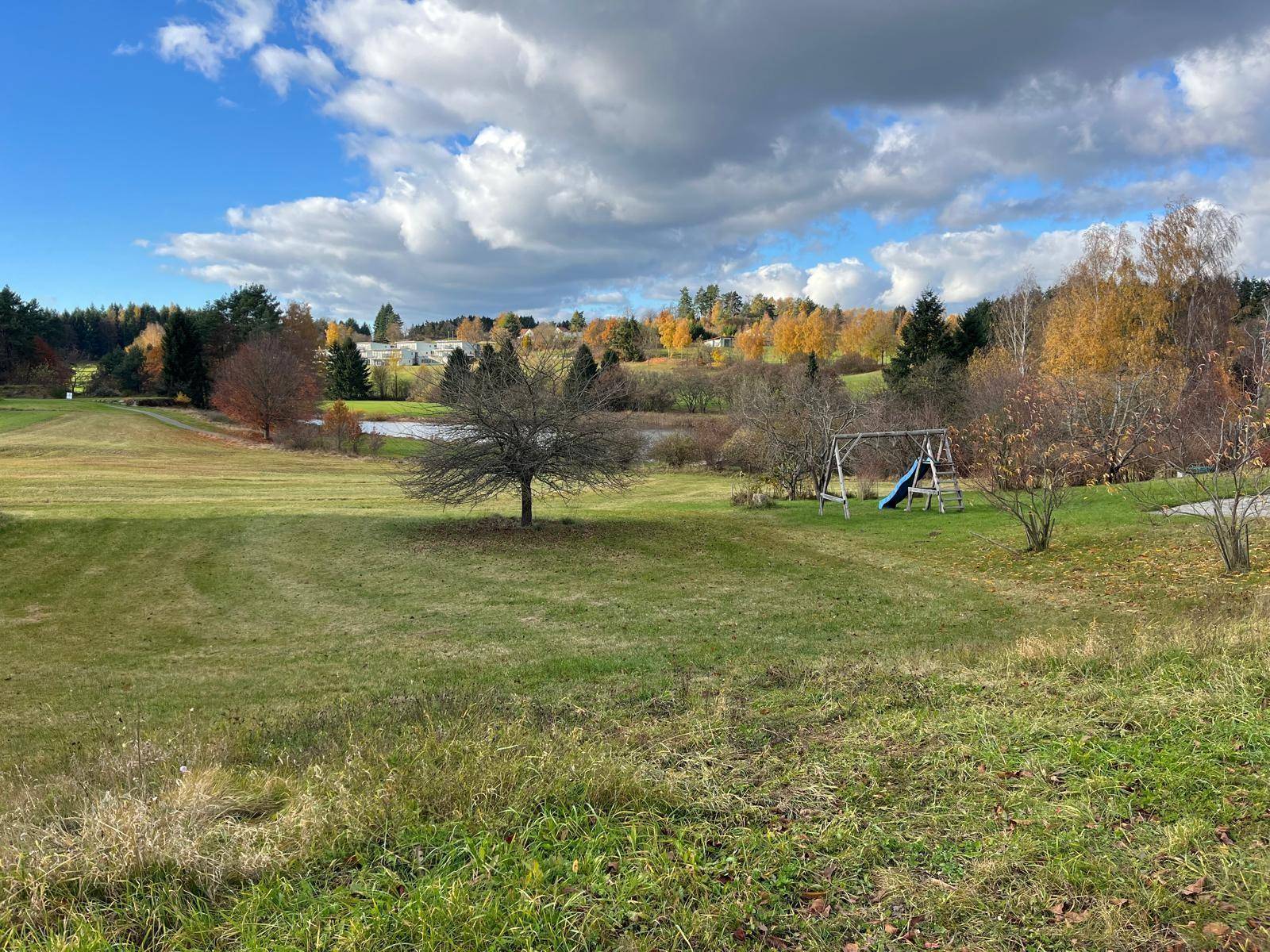 Großer Garten mit Rasenfläche, Bäumen, Teichblick und einem Kinderspielgerät.