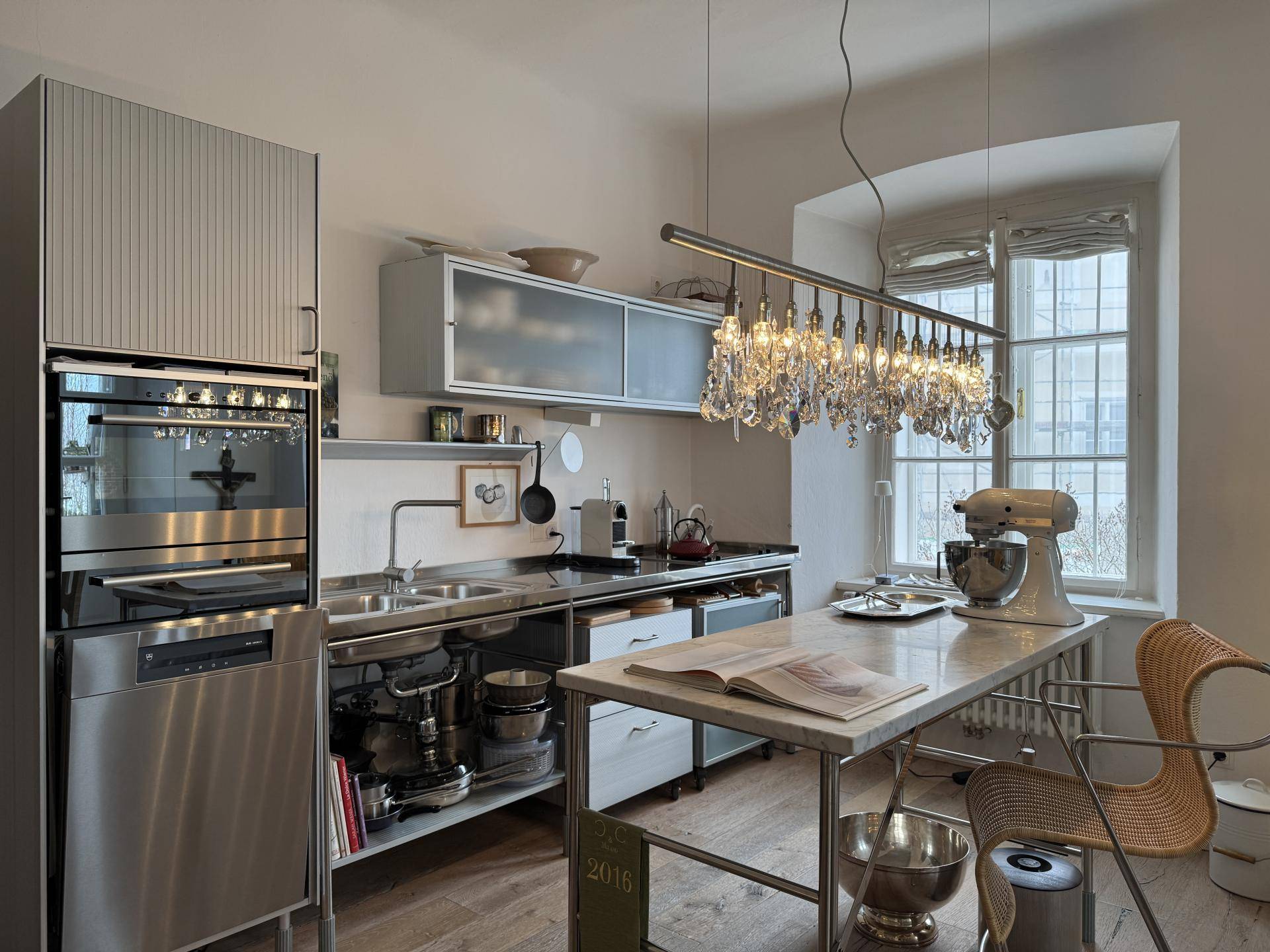 Moderne Küche mit Edelstahloberflächen, Einbaugeräten und eleganter Kristallleuchte.
