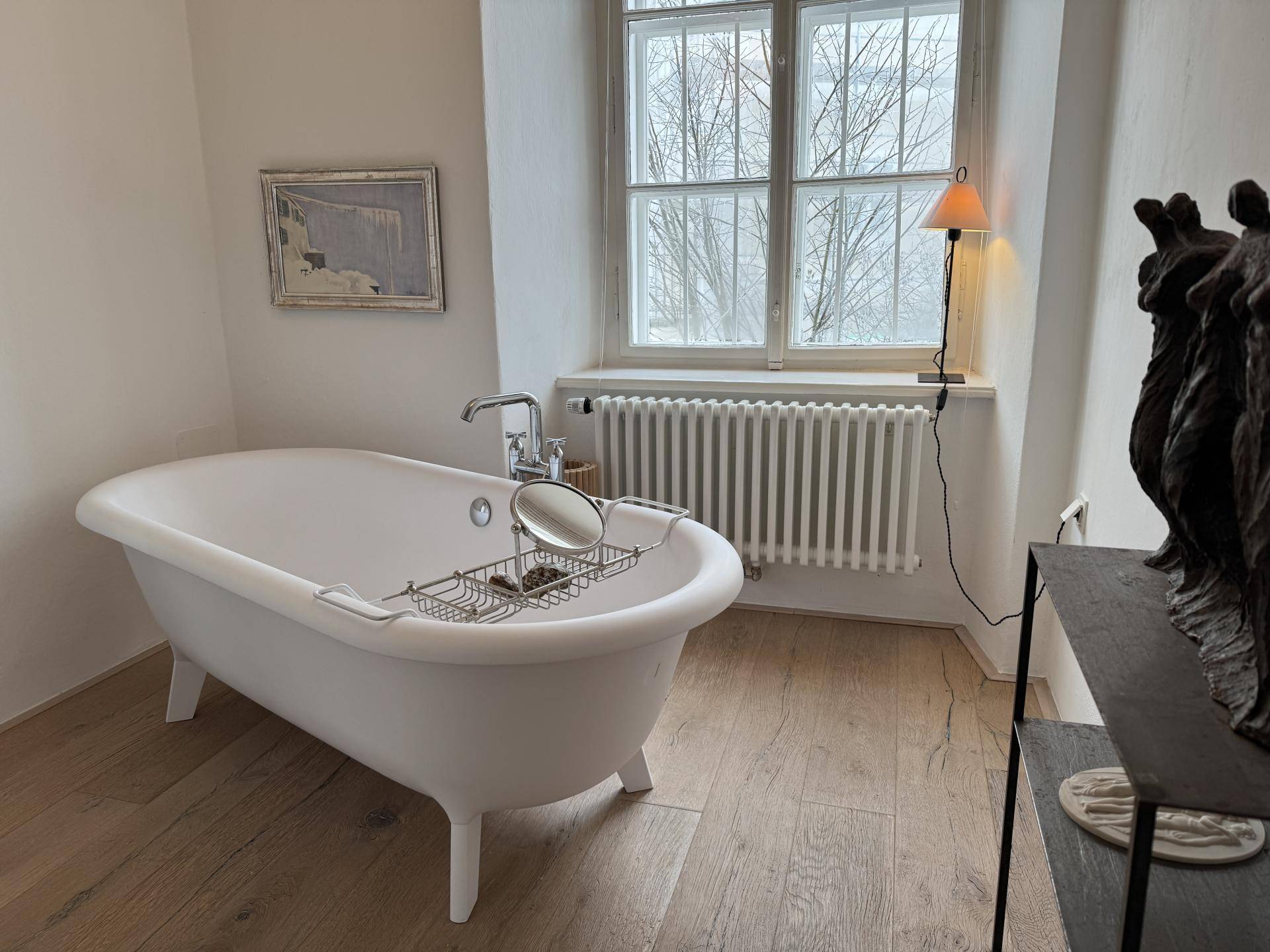 Elegantes Badezimmer mit freistehender Badewanne, Holzboden und großem Fenster.