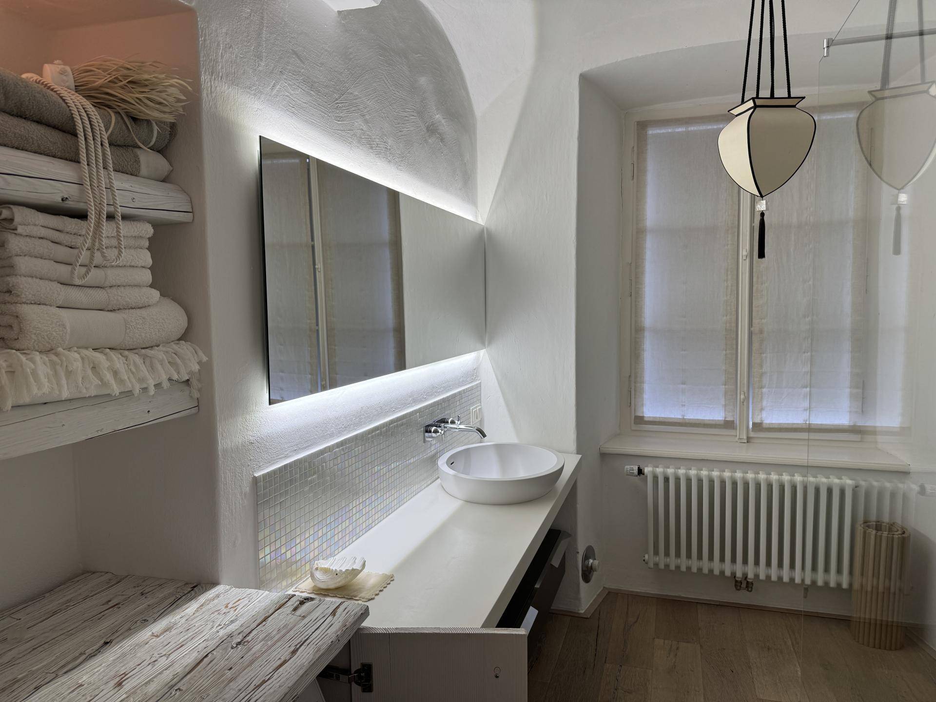 Modernes Badezimmer mit beleuchtetem Spiegel, Aufsatzwaschbecken und Holzboden.