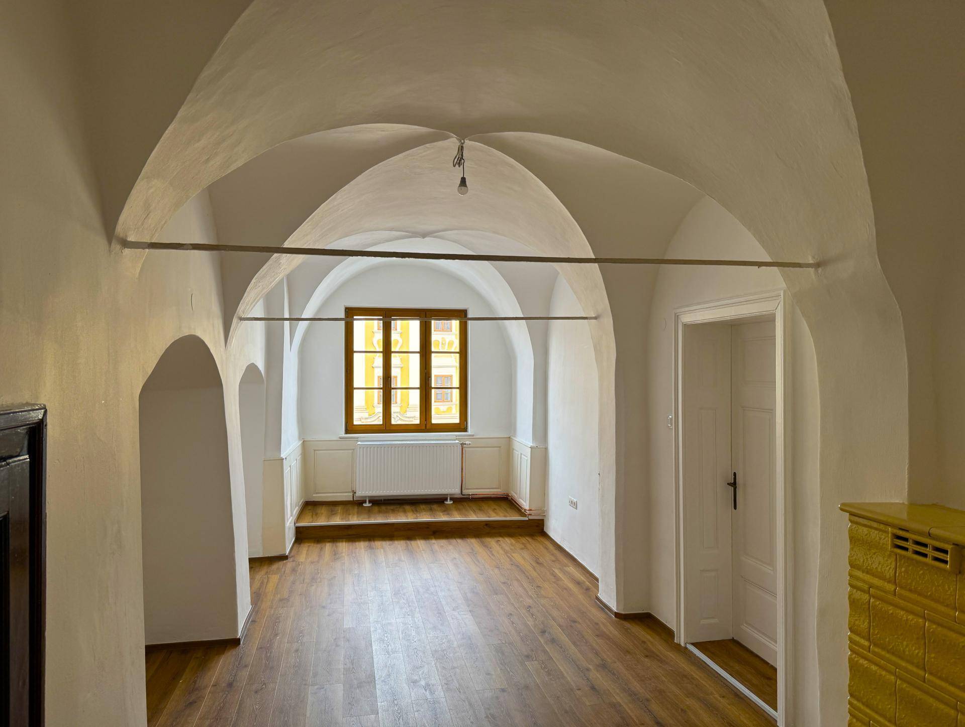 Heller Raum mit beeindruckendem Gewölbedecken, Holzboden und einem Fenster, das viel Tageslicht hereinlässt.