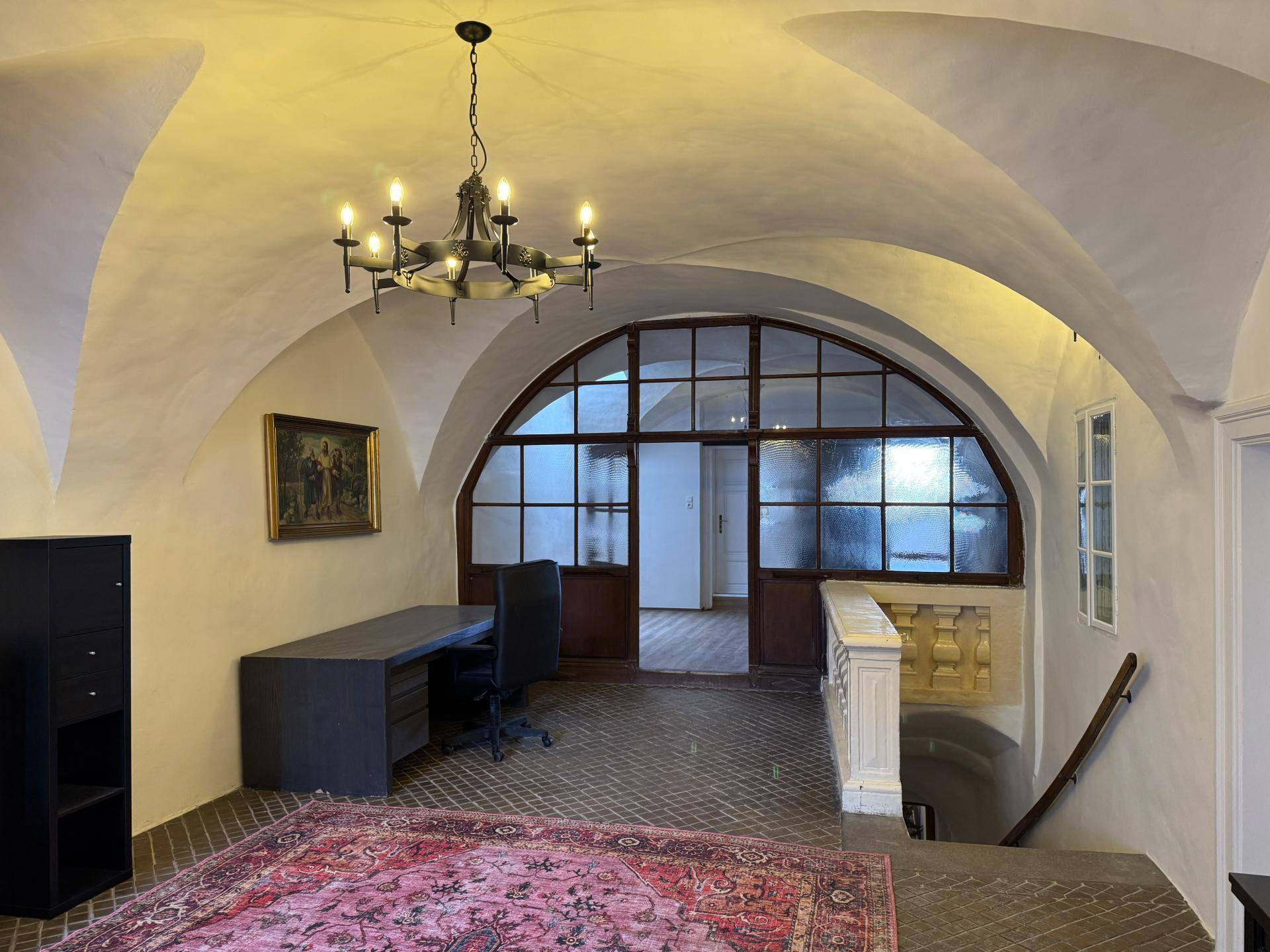 Büro mit Gewölbedecke, gemustertem Teppich und einer großen, bogenförmigen Glastrennwand, die Licht spendet.