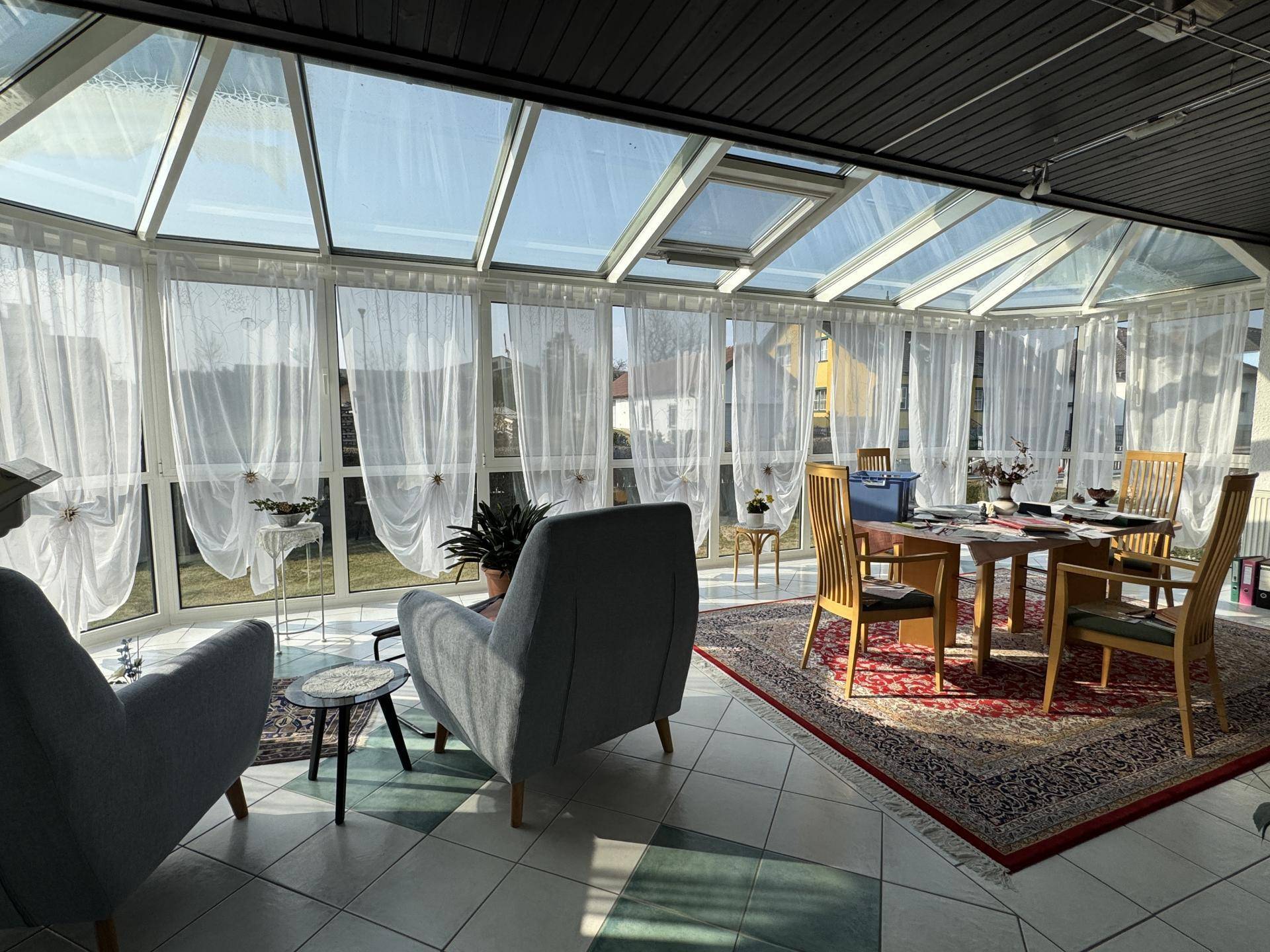 Heller Wintergarten mit Glasdach, Essbereich und gemütlichen Sesseln, ideal für entspannte Stunden.