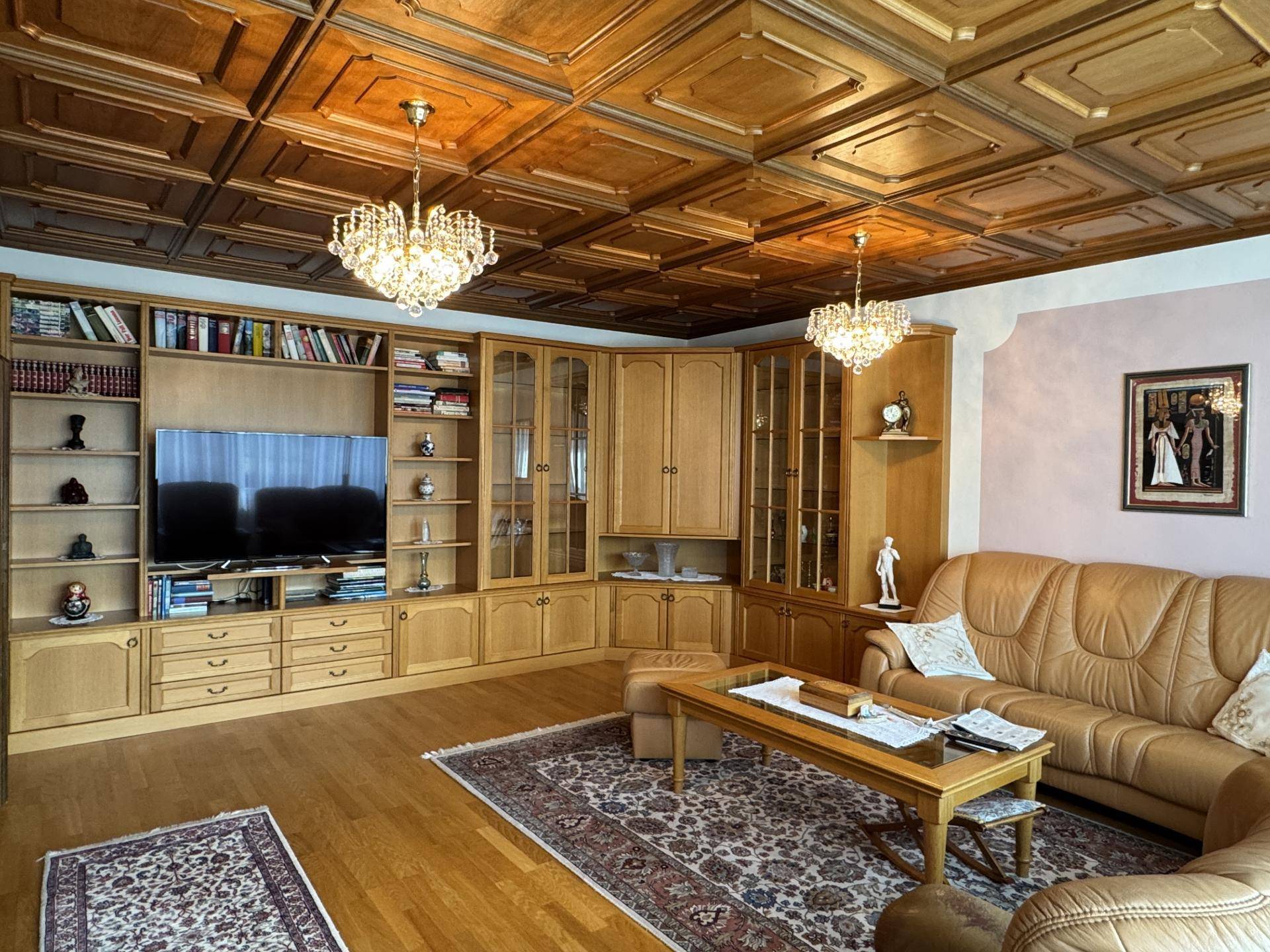 Großzügiges Wohnzimmer mit Holzkassettendecke, Ledersofa und umfangreicher Bücherwand.