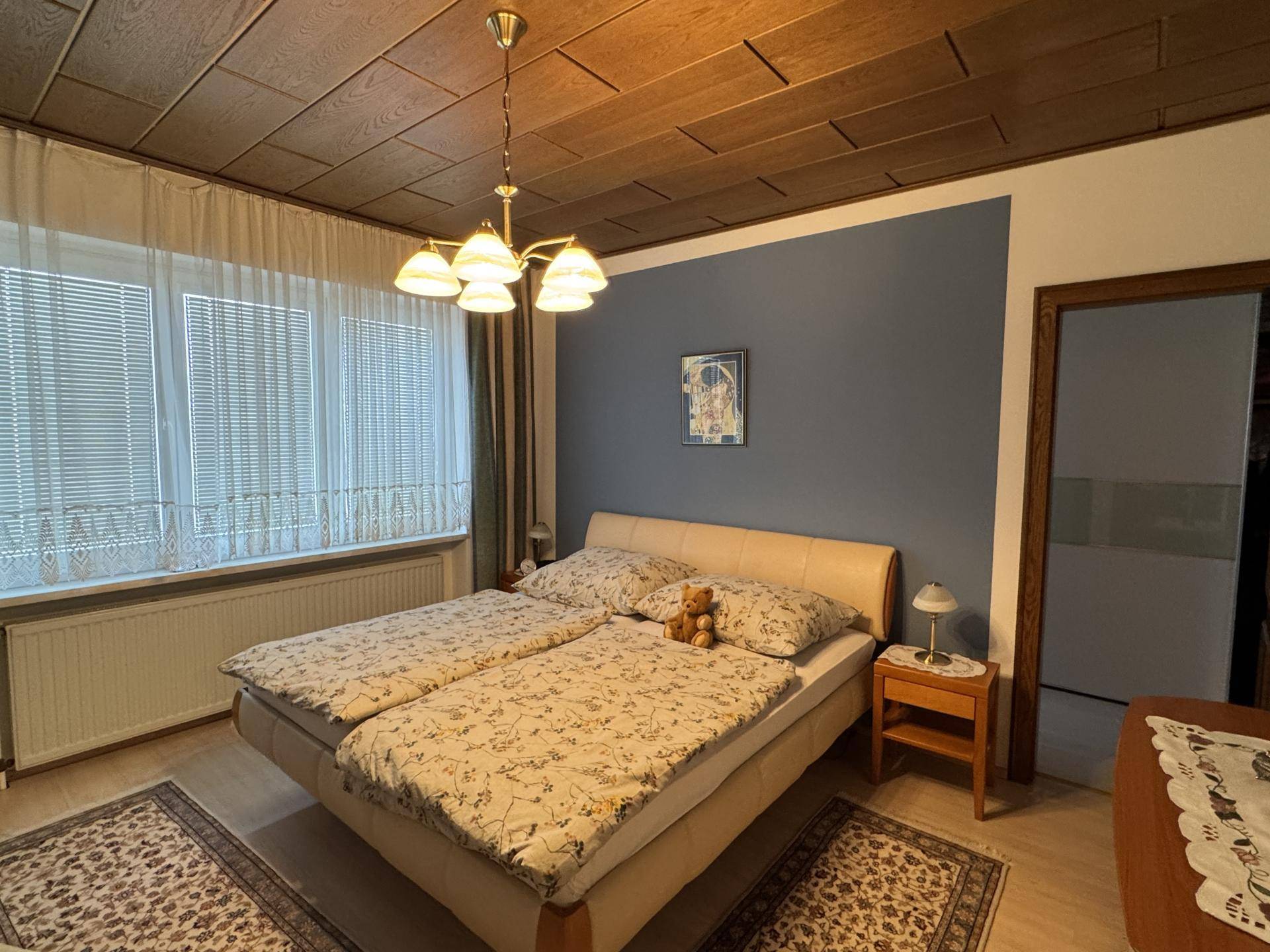 Helles Schlafzimmer mit Doppelbett, Holzdecke und Fenster mit Jalousien für angenehme Lichtverhältnisse.
