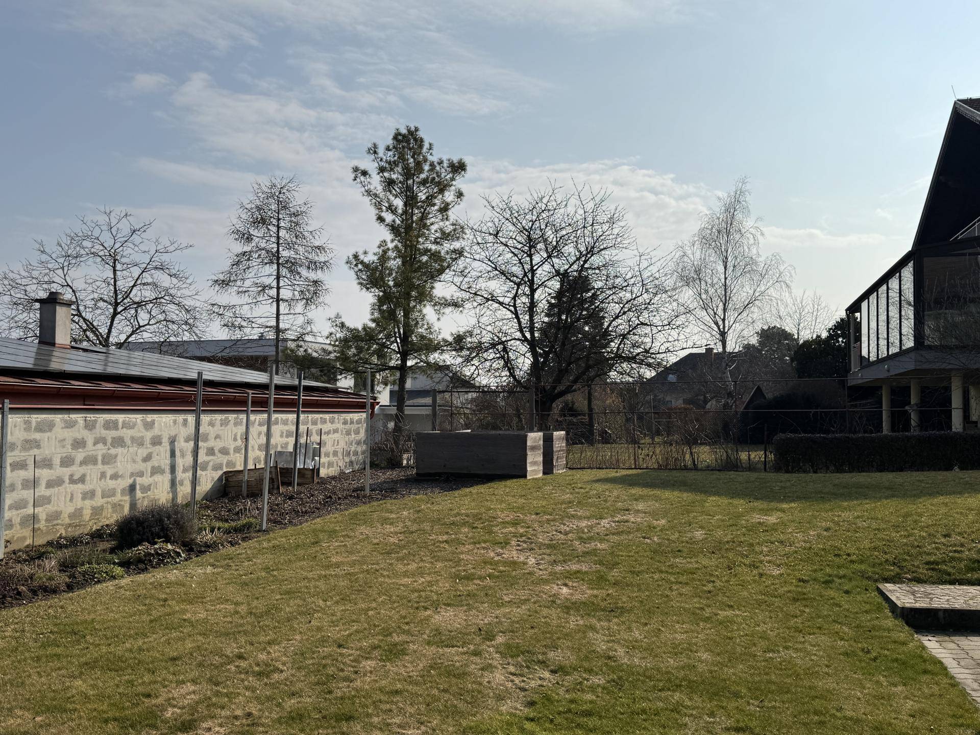 Sonnige Gartenfläche mit Rasen, Bäumen und Blick auf die Umgebung, inklusive Photovoltaikanlage.
