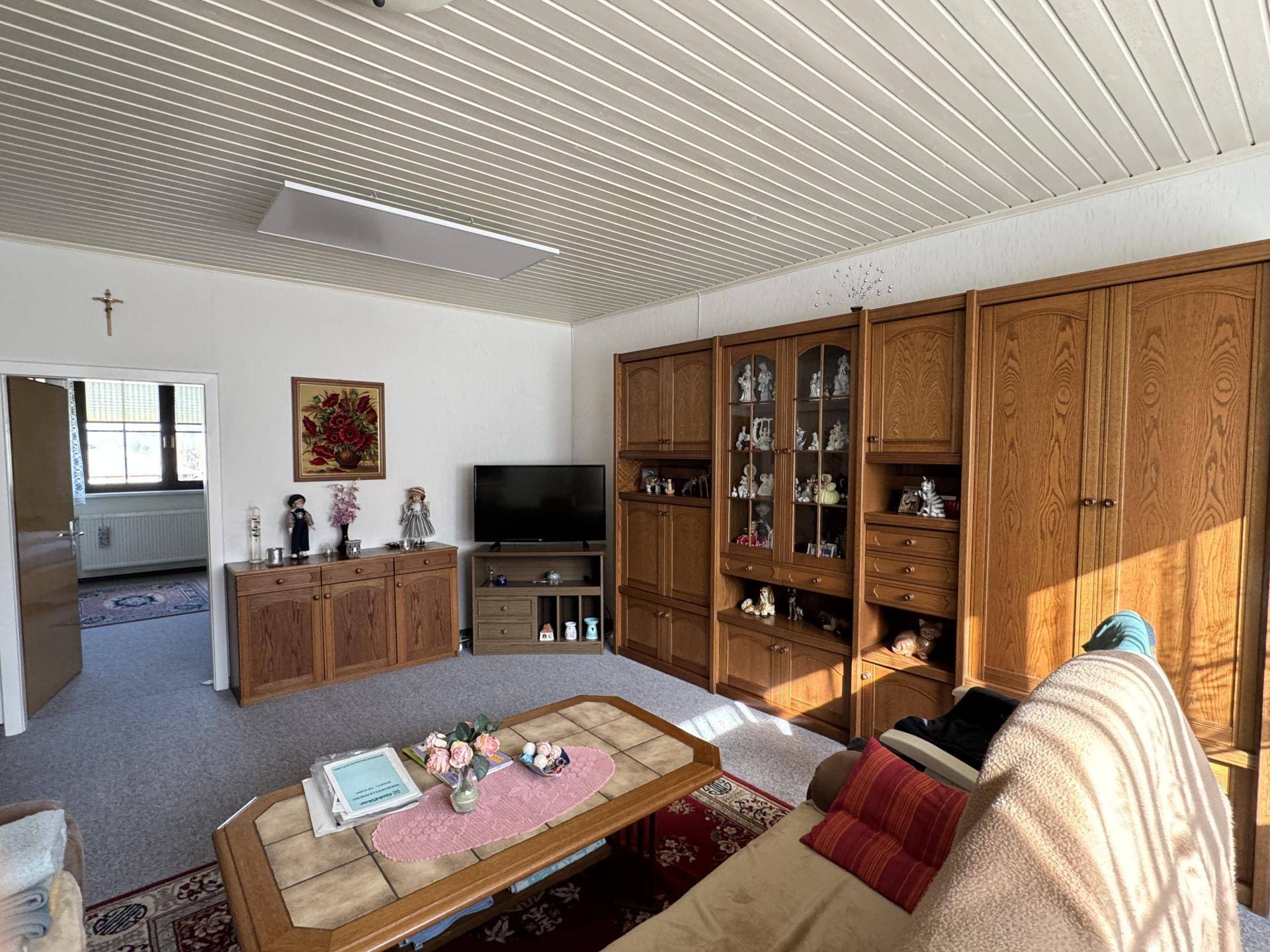 Geräumiges Wohnzimmer mit traditionellen Holzmöbeln, Teppichboden und heller Decke.