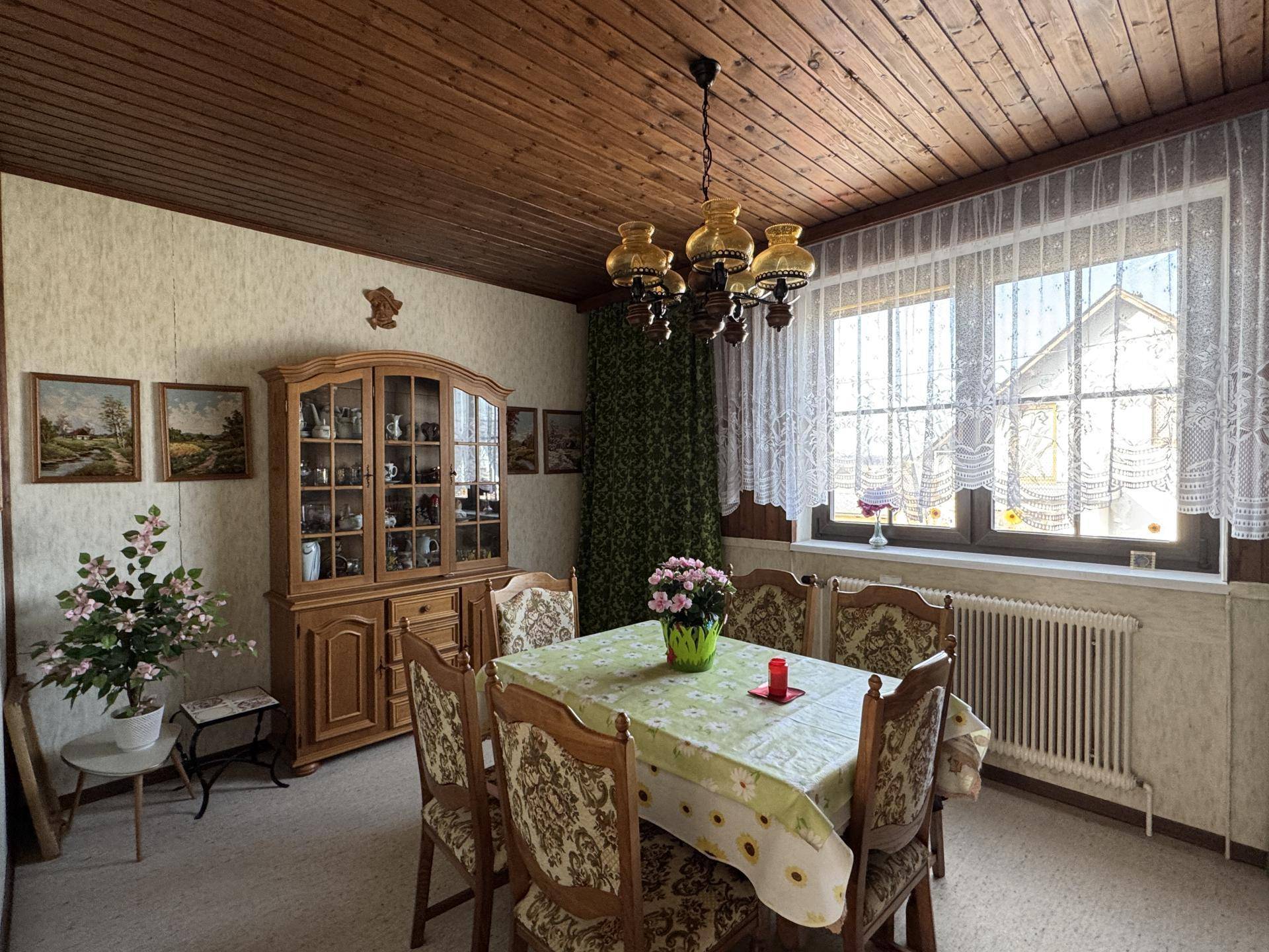 Traditioneller Essbereich mit Holzmöbeln, Holztäfelung an der Decke und großem Fenster.