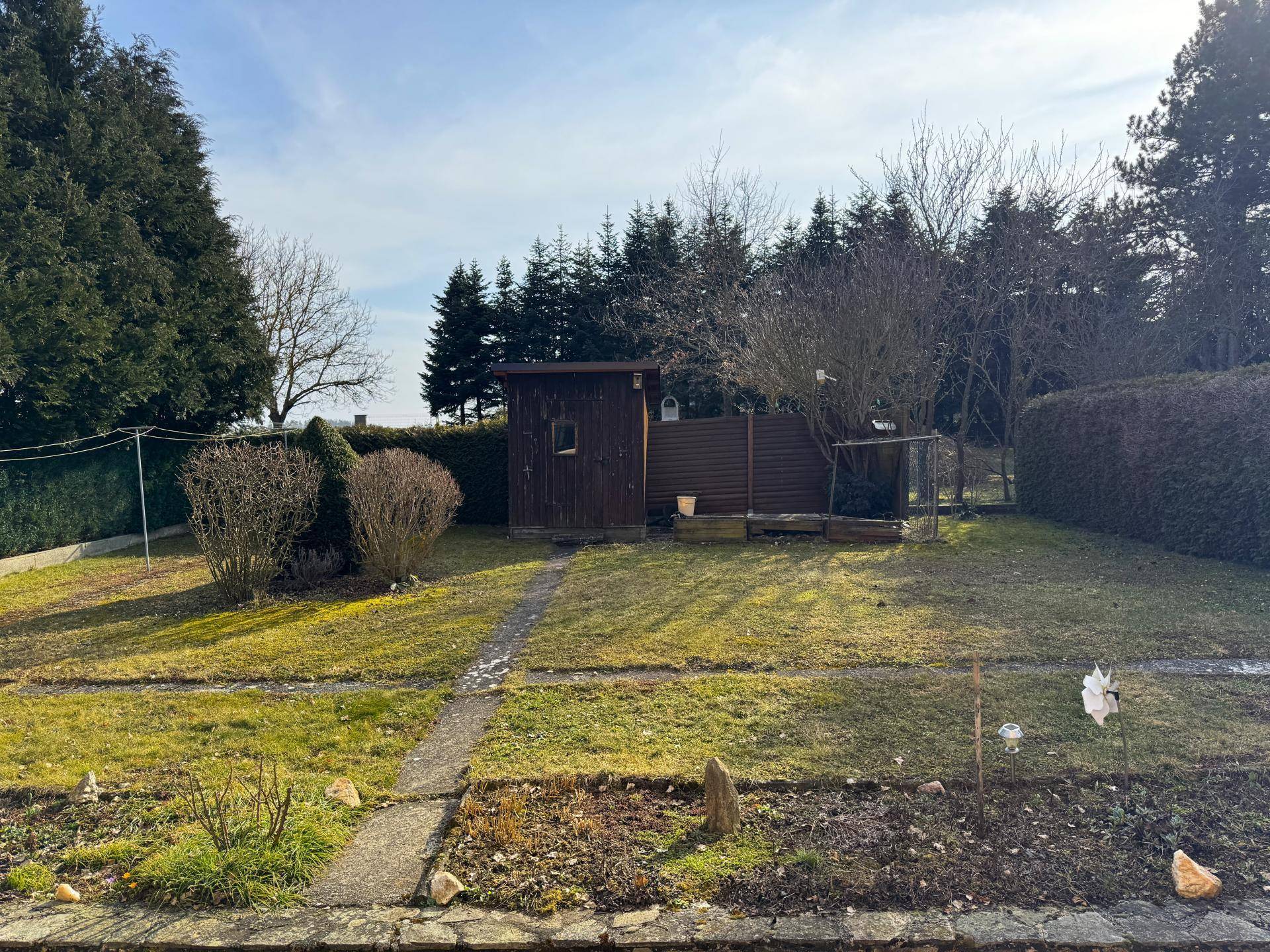 Großer Gartenbereich mit Rasenfläche, Gartenhaus und hohen Bäumen im Hintergrund.