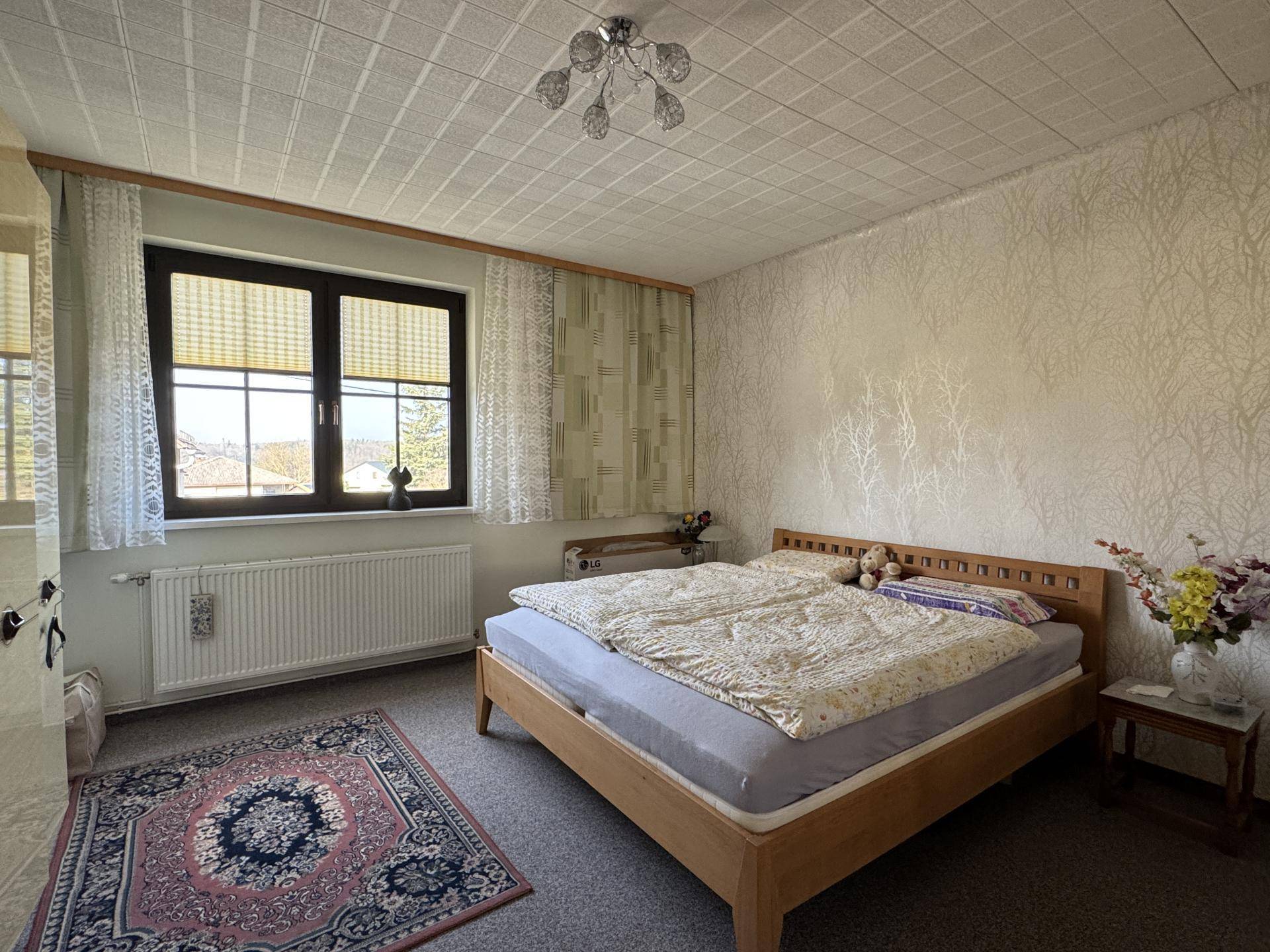 Helles Schlafzimmer mit Doppelbett, Teppichboden und Fenster mit Blick ins Grüne.