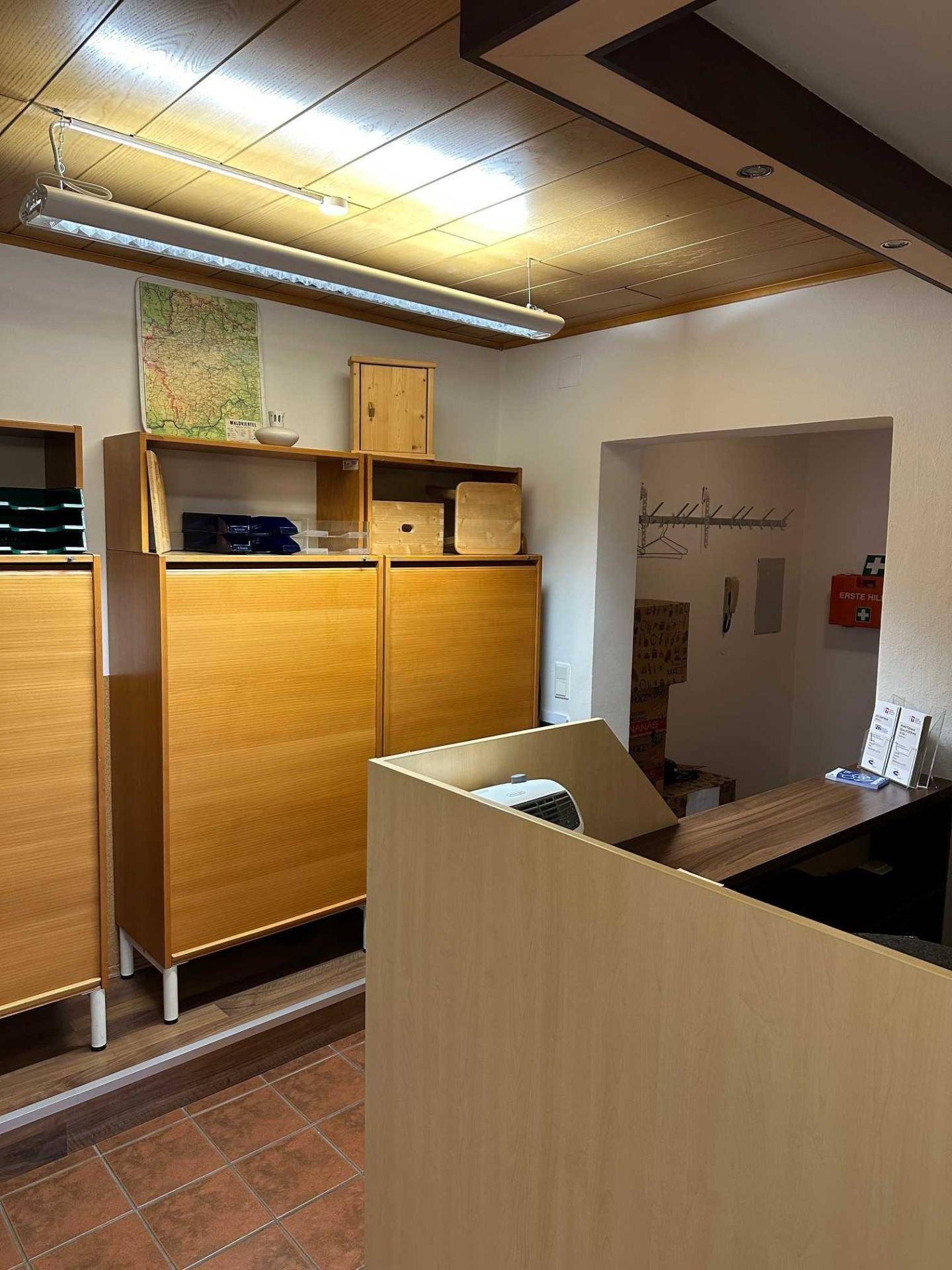 Empfangsbereich mit Holzschränken, einem Schreibtisch und Terrakottafliesen, gut beleuchtet.