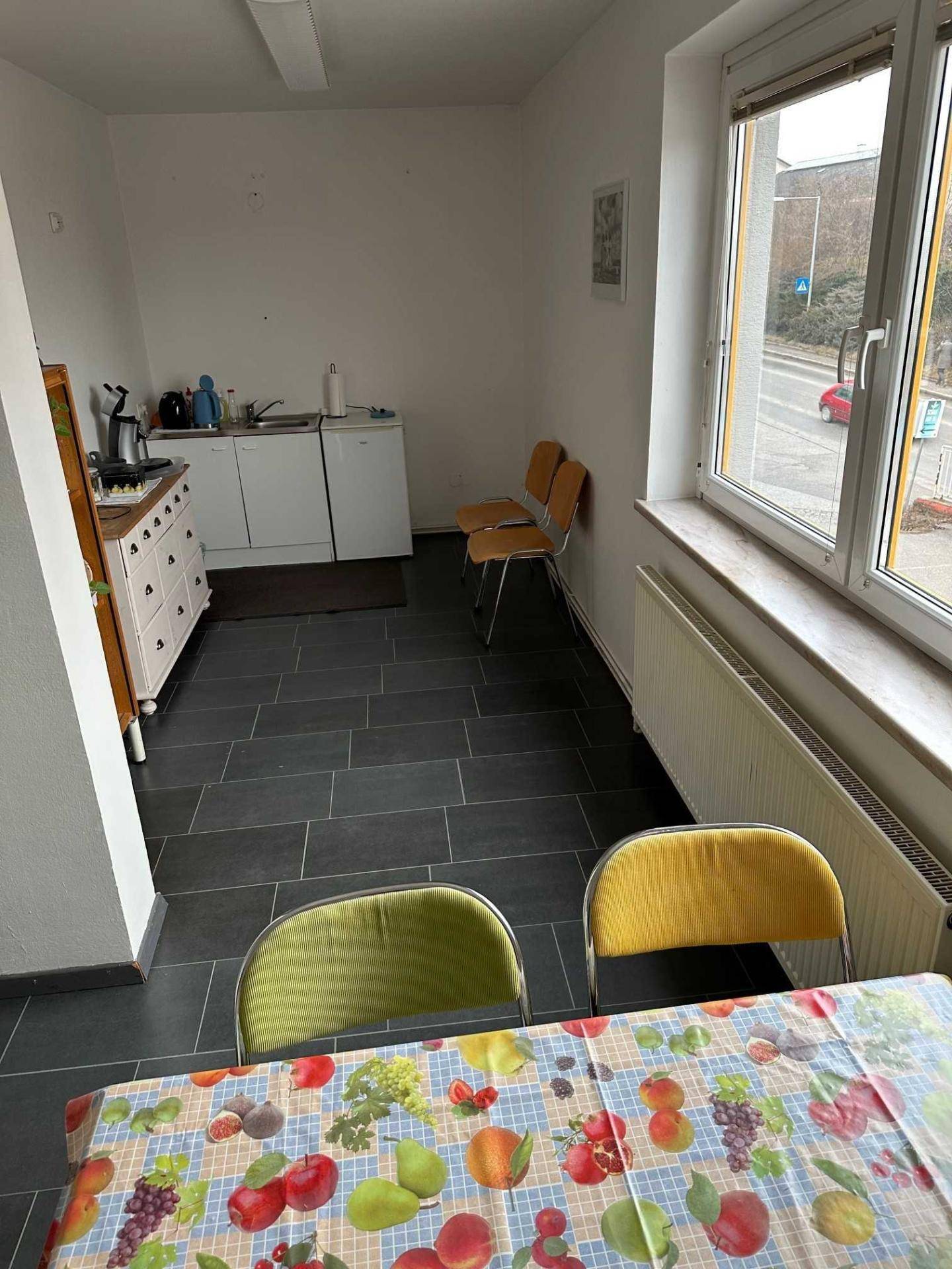 Funktionale Küchenzeile mit dunklen Fliesen, Spüle und Kühlschrank, ergänzt durch einen kleinen Essbereich.