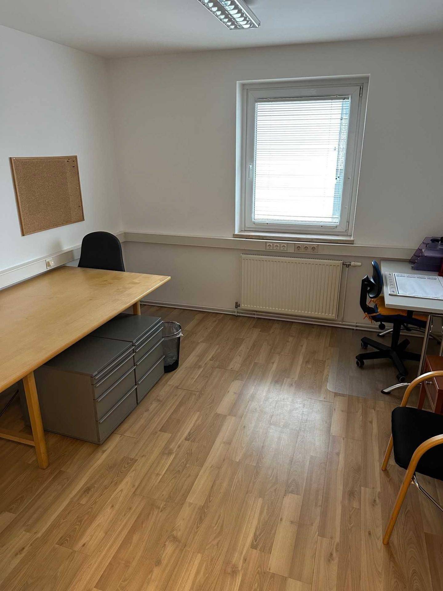 Einfaches Büro mit einem langen Schreibtisch, Bürostühlen und einem Aktenschrank, mit Laminatboden.