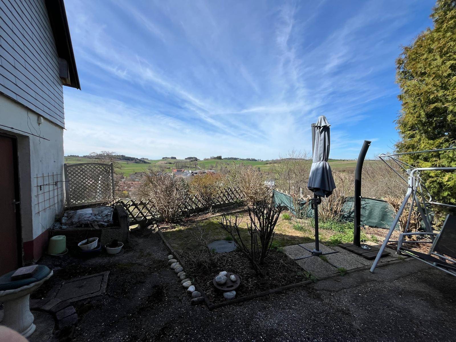 Gartenbereich mit Sonnenschirm und weitem Blick über die hügelige Landschaft.