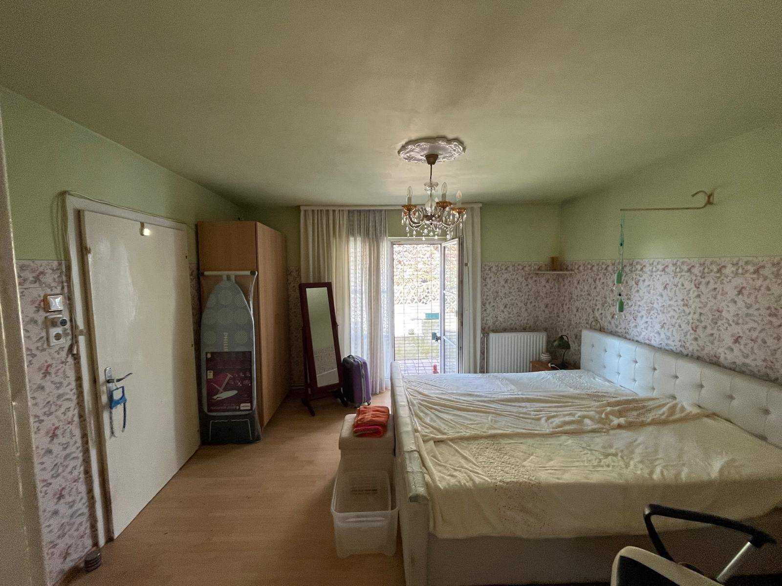 Schlafzimmer mit grün gestrichenen Wänden, gemusterter Tapete und Zugang zu einem Außenbereich.