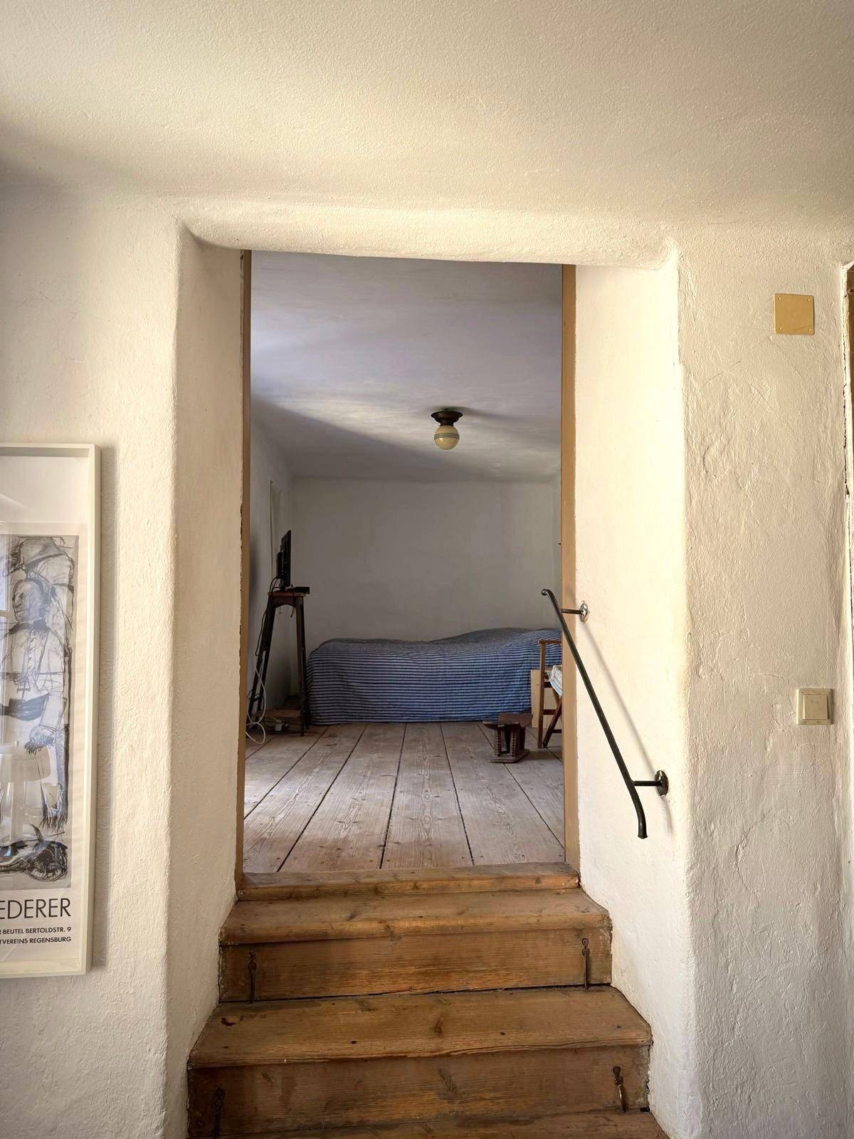 Treppenaufgang mit Holzstufen, der zu einem hellen Schlafzimmer mit Holzboden führt.
