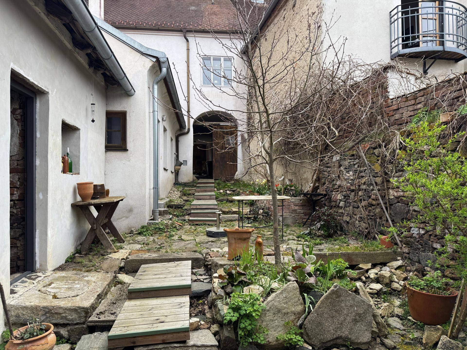 Rustikaler Innenhof mit Steinstufen, üppiger Vegetation und einem kleinen Balkon im Hintergrund.