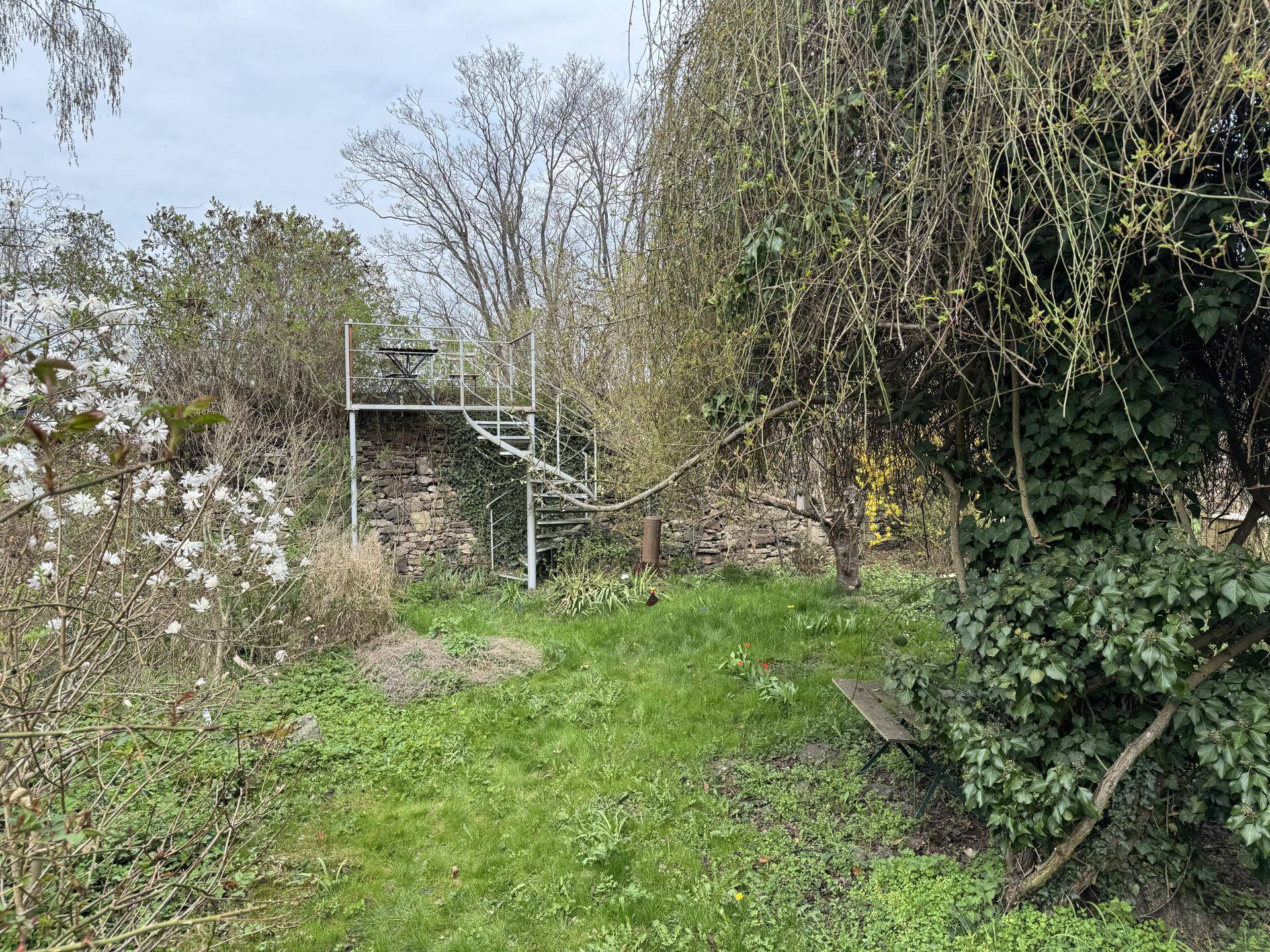 Naturbelassener Garten mit einer freistehenden Wendeltreppe, die zu einer erhöhten Plattform führt.