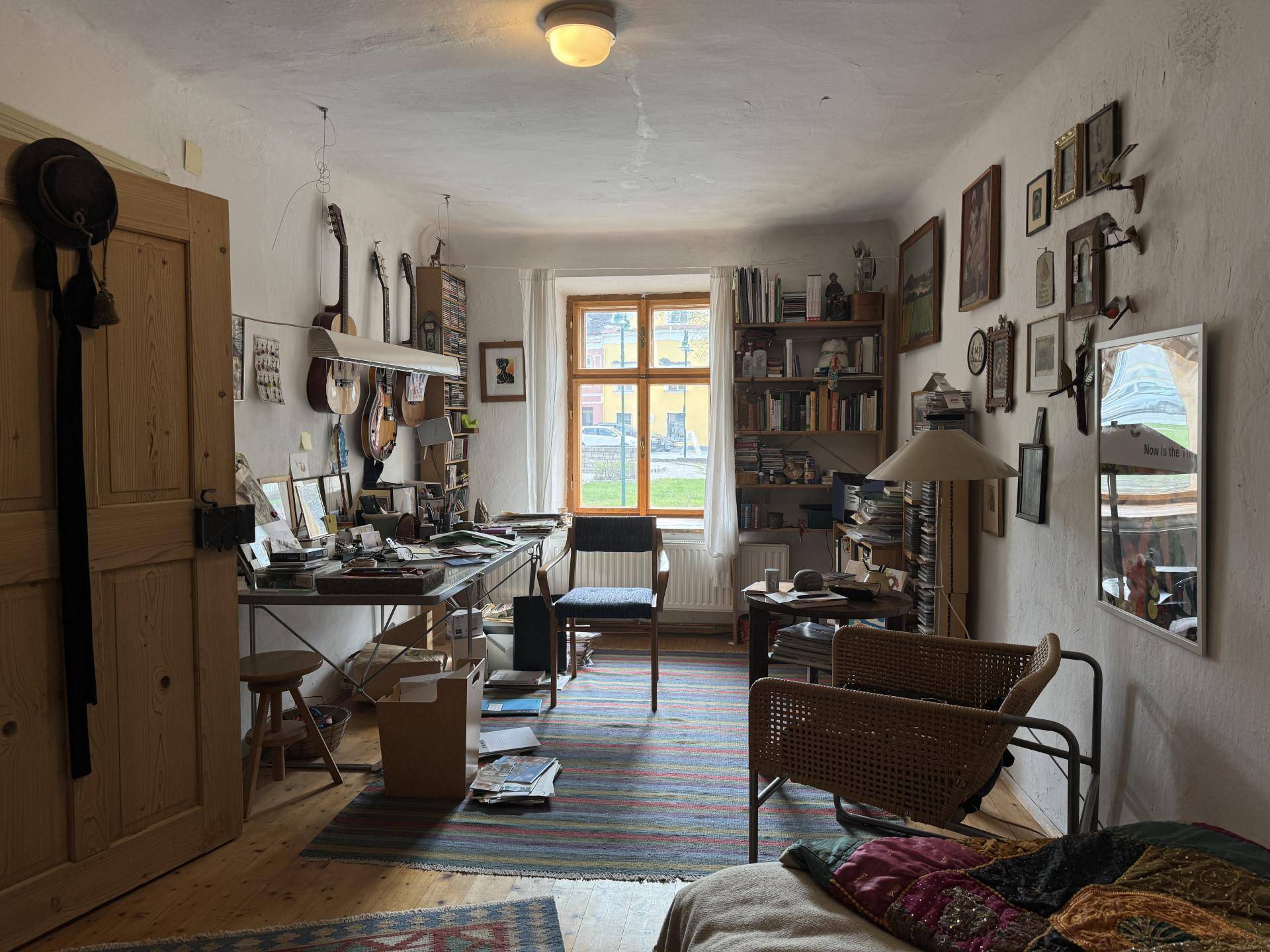 Helles Arbeitszimmer mit Holzboden, Bücherregalen und einem Schreibtisch voller persönlicher Gegenstände.