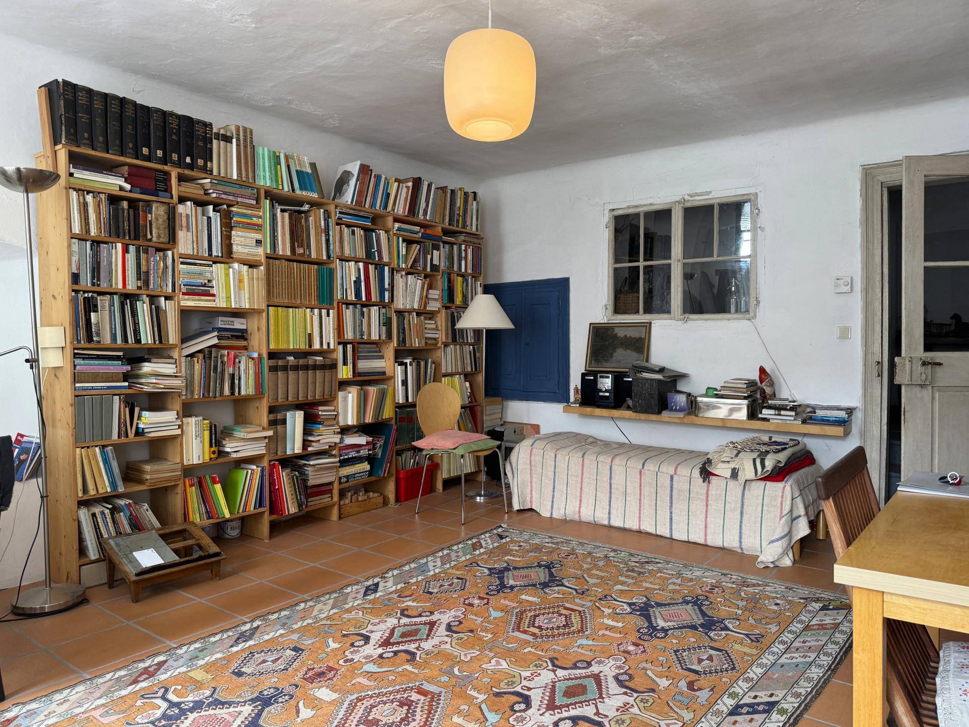 Wohnbereich mit umfangreicher Bibliothek, einem Tagesbett und einem großen Teppich auf Terrakottaboden.