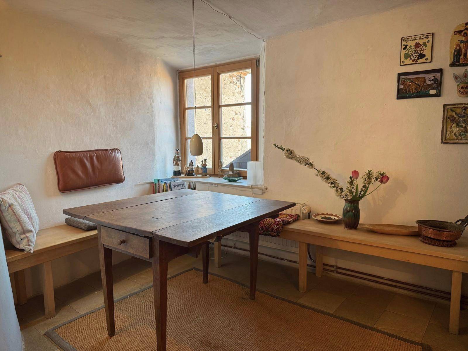 Gemütlicher Essbereich mit Holztisch, Sitzbänken und einem Fenster, das viel Tageslicht hereinlässt.