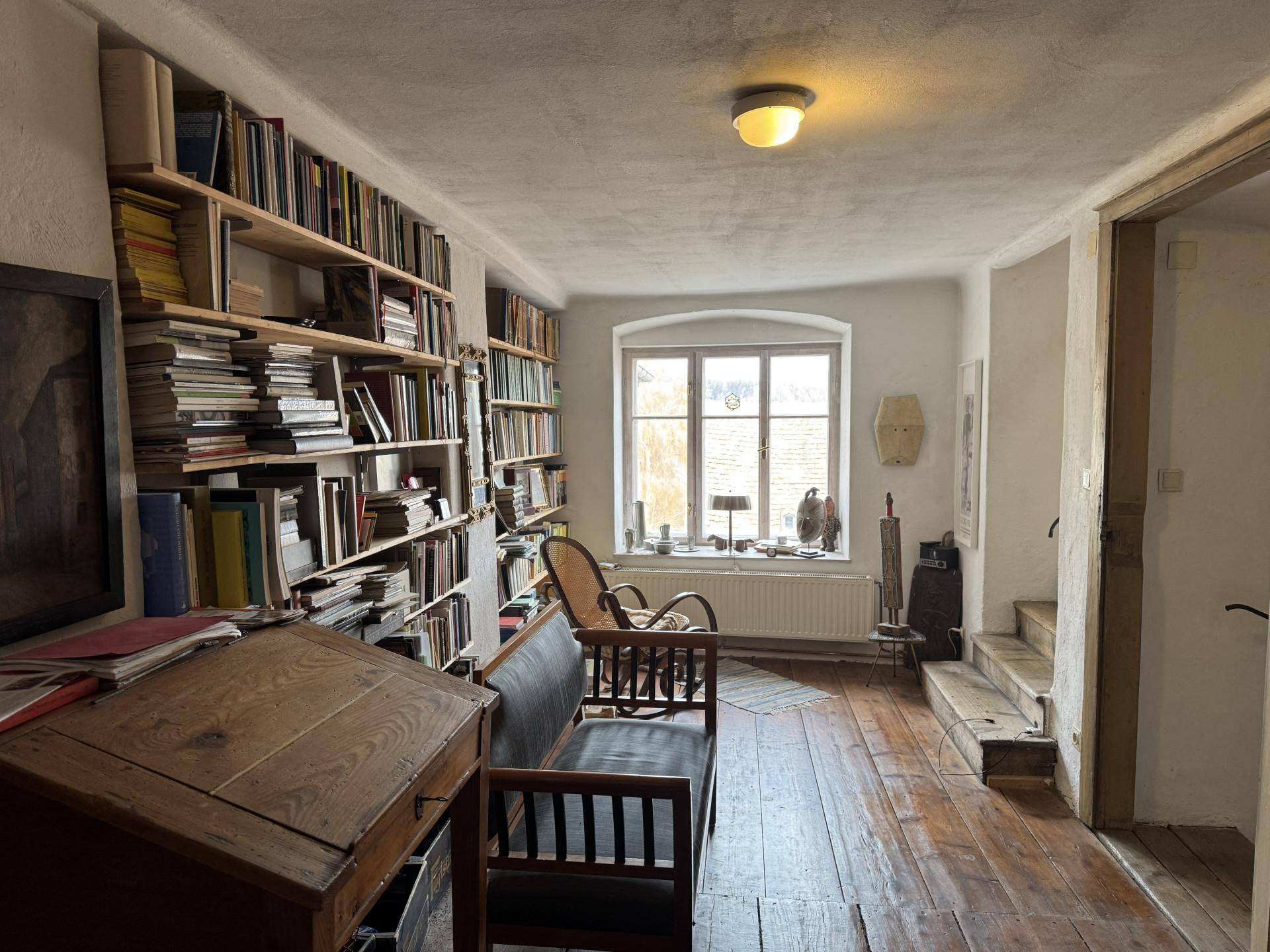 Langer Flur mit Holzdielenboden, Bücherregalen und einem Fenster, das den Raum erhellt.