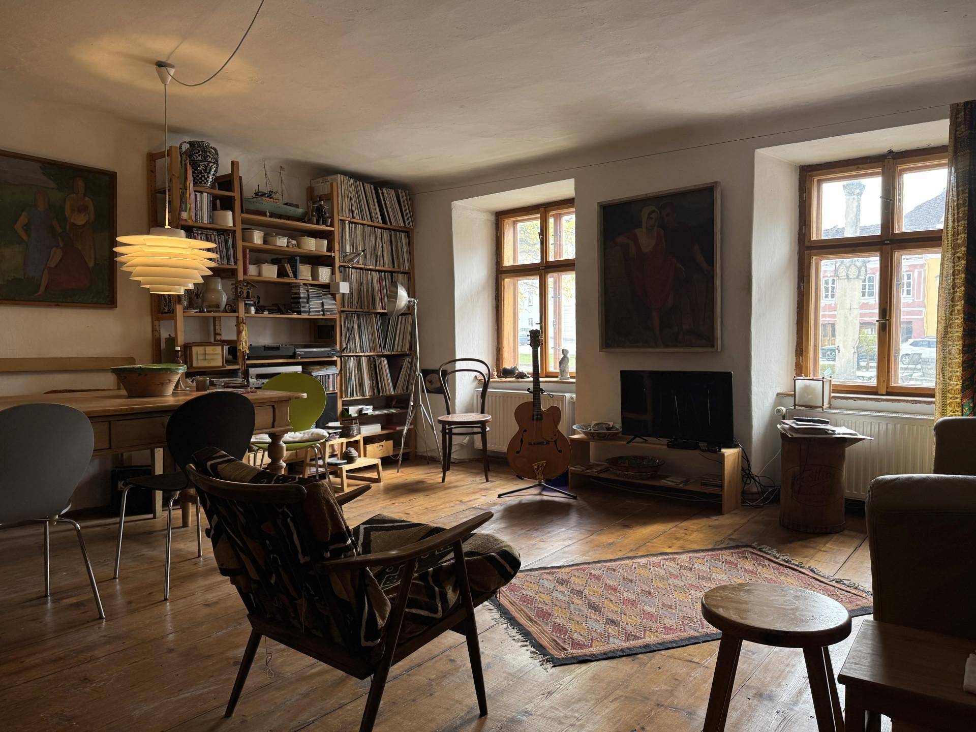 Helles Wohnzimmer mit Holzdielenboden, verschiedenen Sitzgelegenheiten und Kunstwerken an den Wänden.