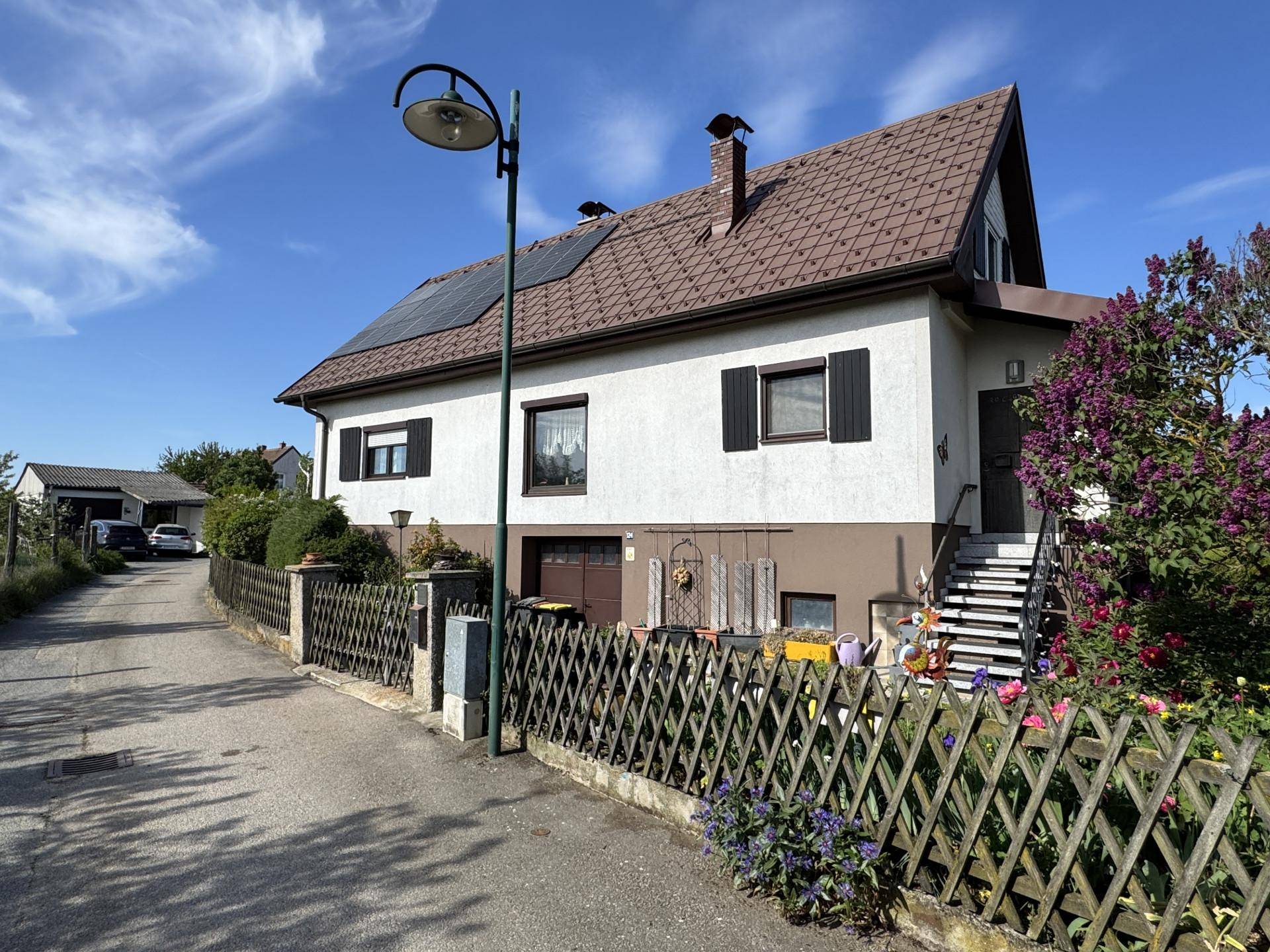 Seitenansicht des Hauses mit Zufahrt, Solaranlage auf dem Dach und Treppenzugang zum Eingangsbereich.