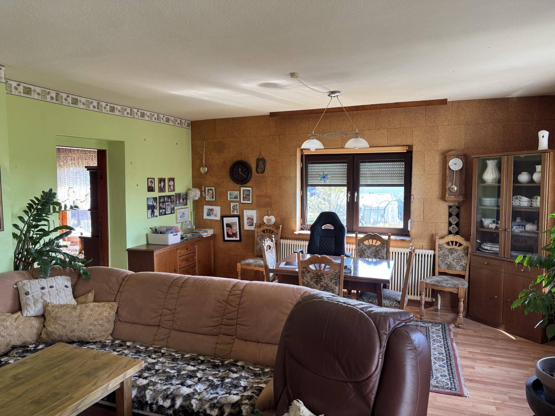 Geräumiger Wohn-Essbereich mit Sofa, Esstisch und Blick ins Grüne durch das Fenster.