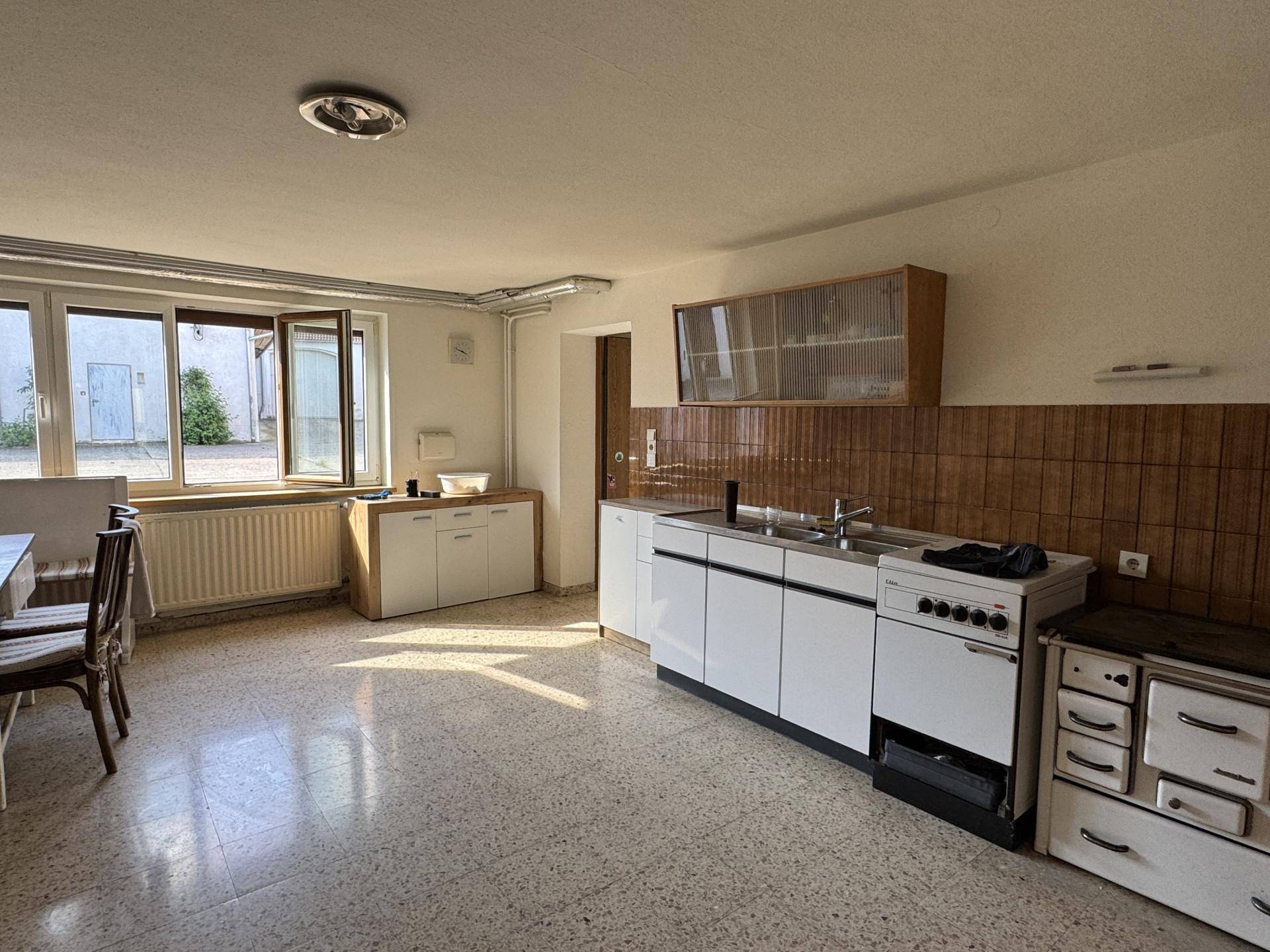 Einfache Küche mit weißen Unterschränken, Terrazzoboden und Zugang zum Außenbereich.
