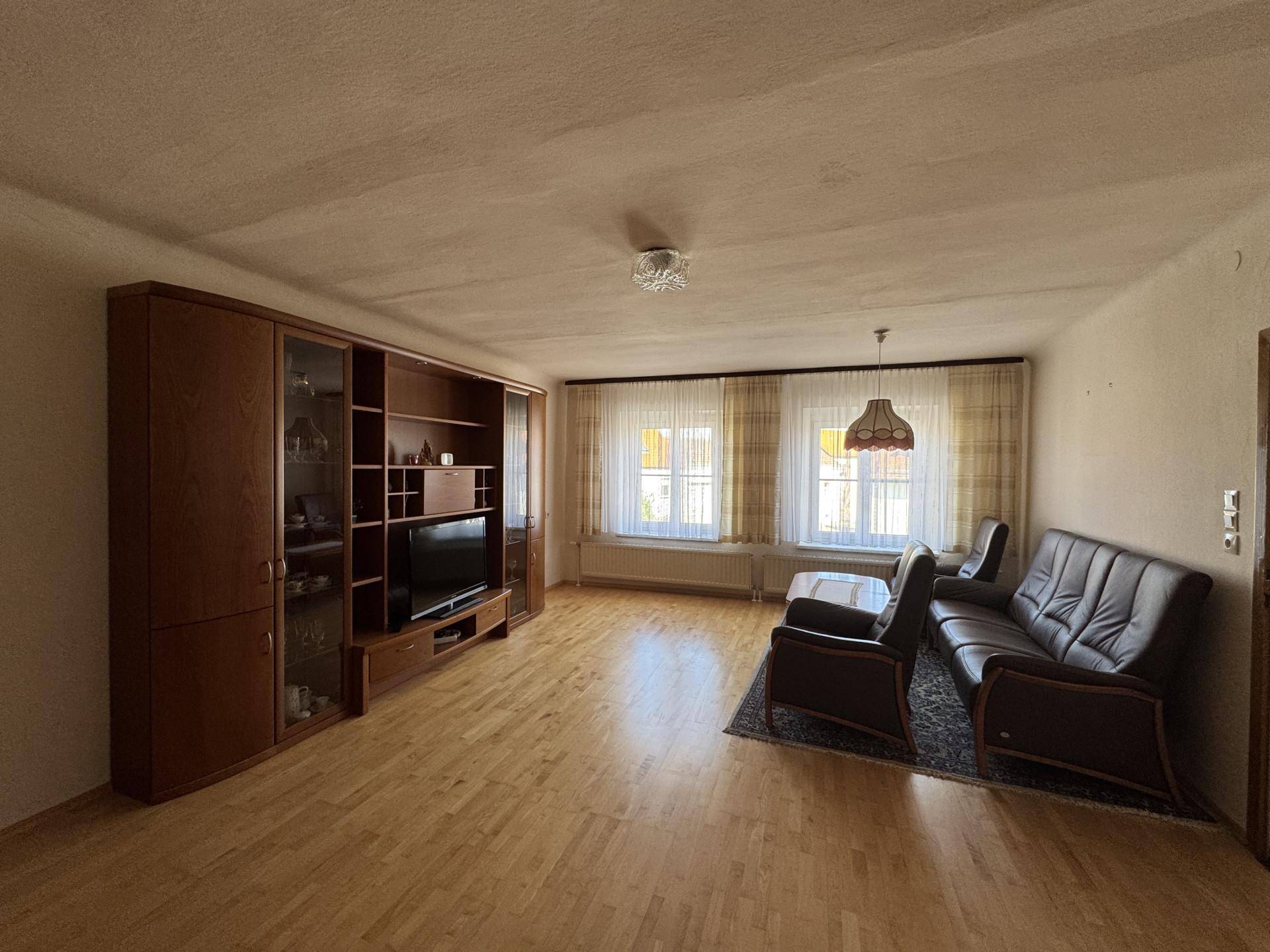 Geräumiges Wohnzimmer mit Holzboden, Ledersofa und großer Schrankwand.