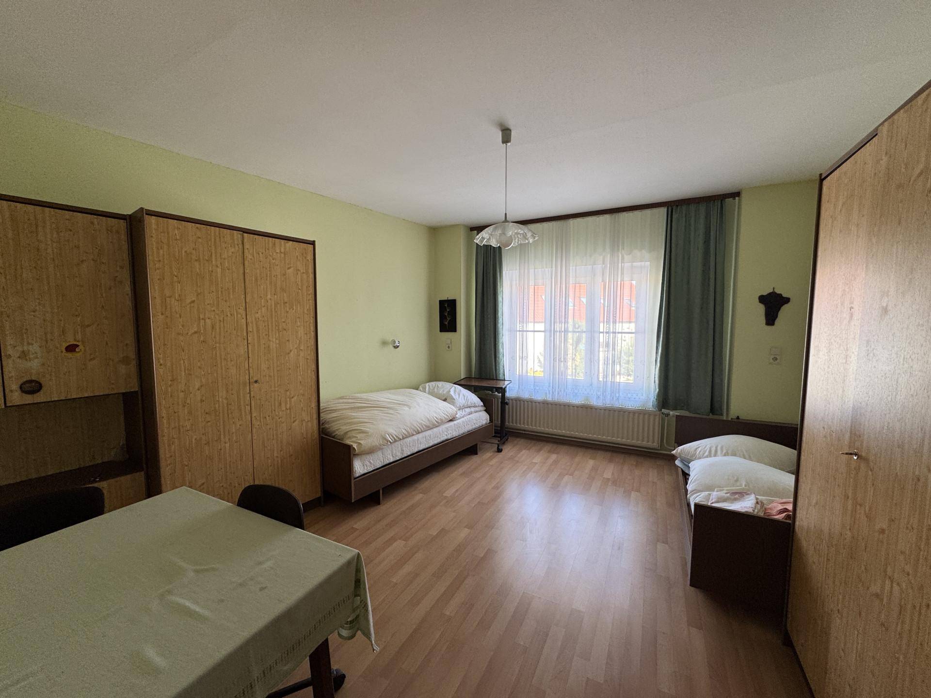 Einfaches Schlafzimmer mit zwei Einzelbetten, Laminatboden und einem Fenster mit Vorhängen.