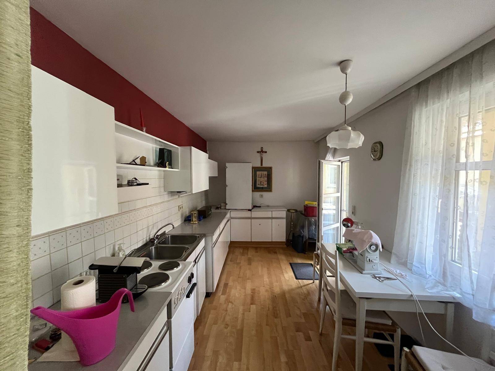 Helle Wohnküche mit weißen Schränken, Esstisch und Fenster mit Vorhängen.