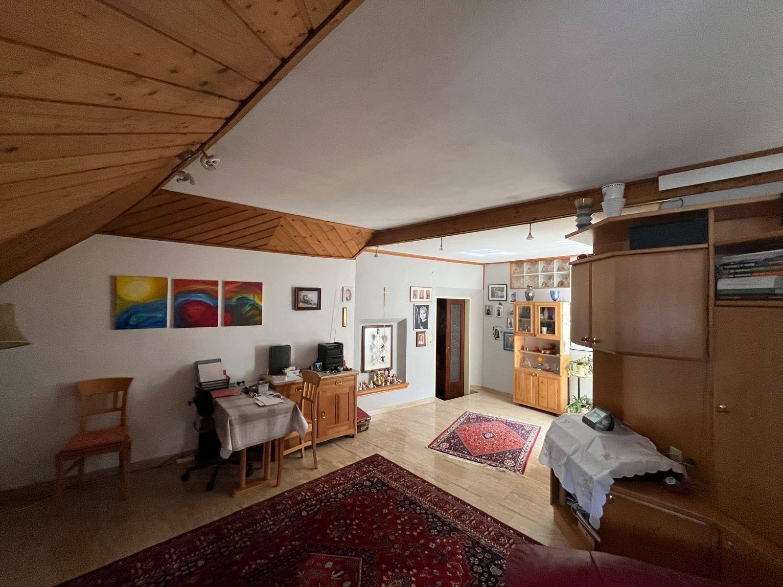 Geräumiges Wohnzimmer mit Holzdachschrägen, Teppichboden und verschiedenen Möbeln.