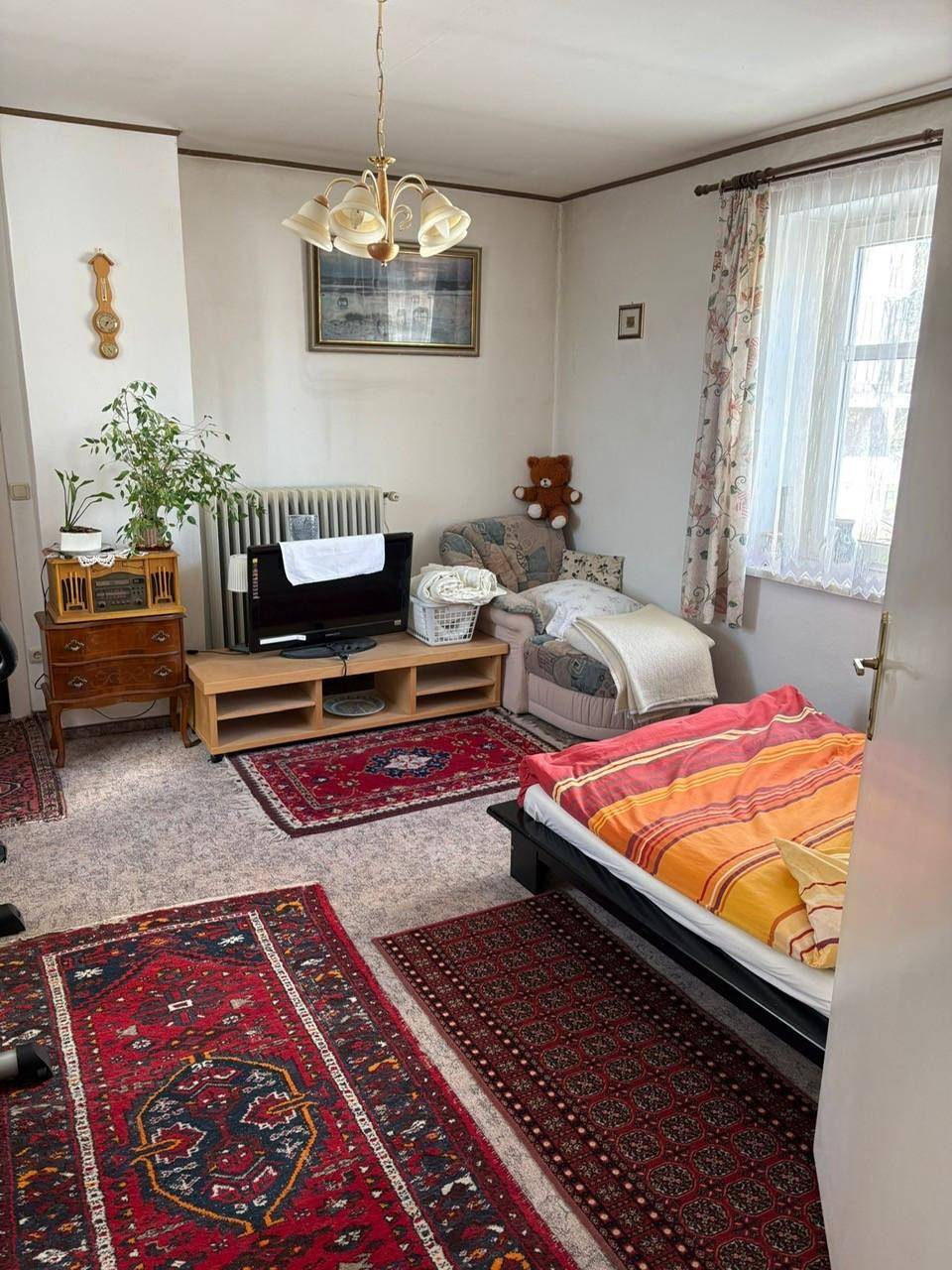 Schlafzimmer mit Teppichboden, Bett, Fernseher und traditionellen Teppichen.