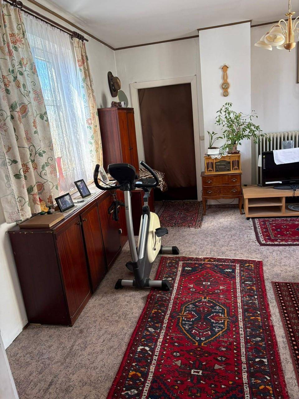 Wohnzimmer mit Teppichboden, Heimtrainer und traditionellen Möbeln.