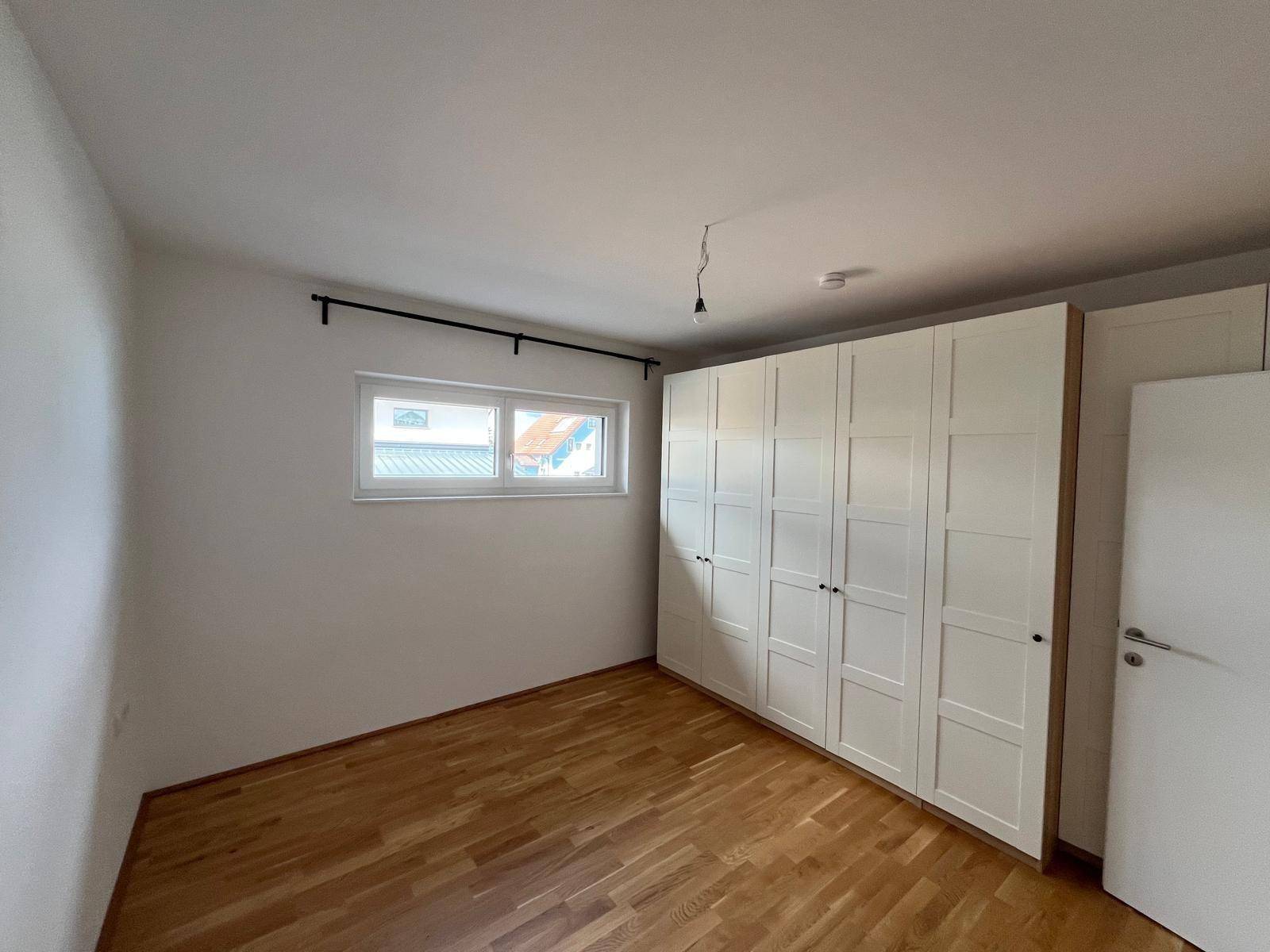 Schlafzimmer mit Holzboden, weißen Wänden und einem großen Kleiderschrank.