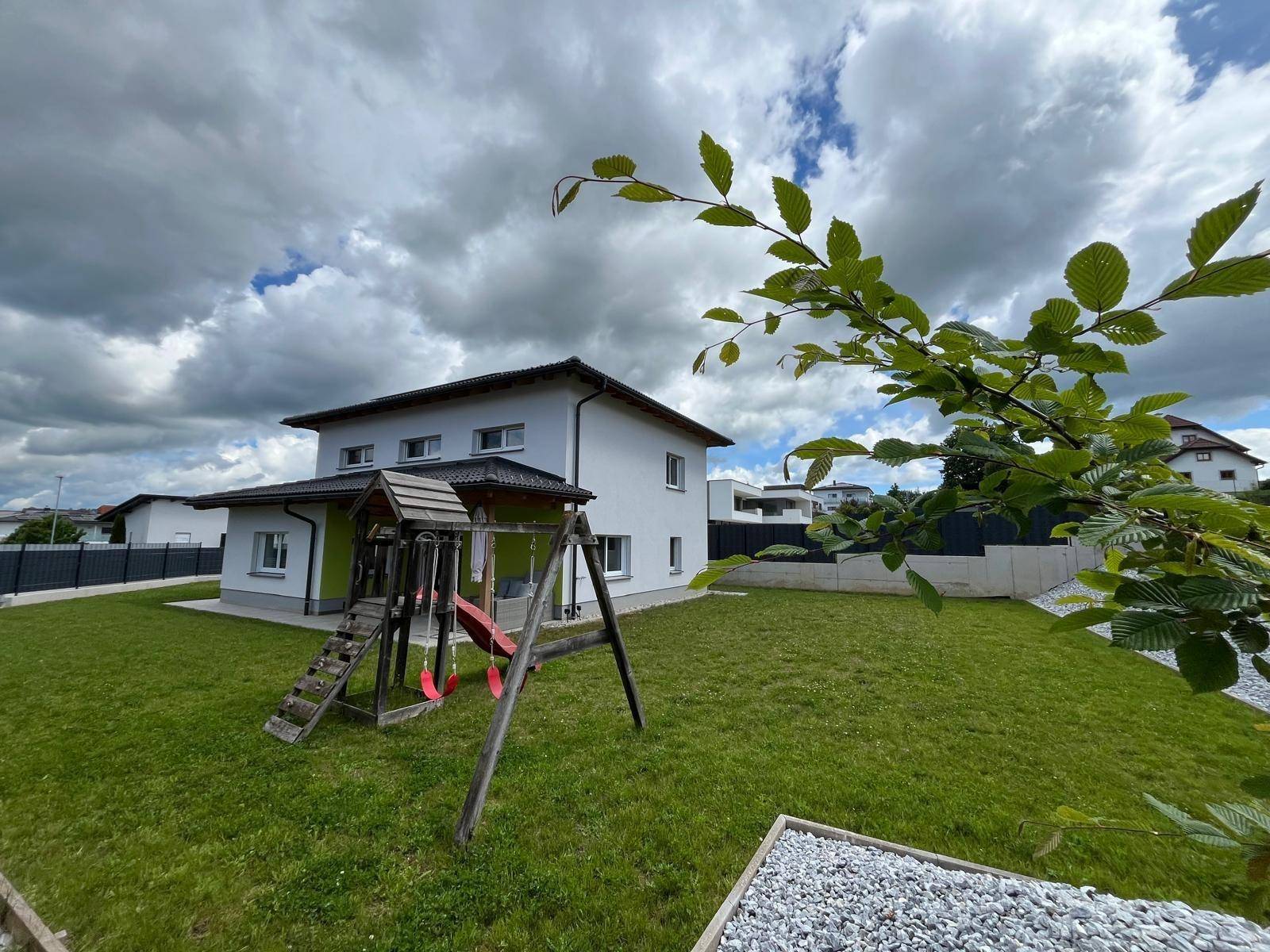 Großzügiger Gartenbereich mit Rasenfläche und einem Holzspielplatz neben dem modernen Einfamilienhaus.