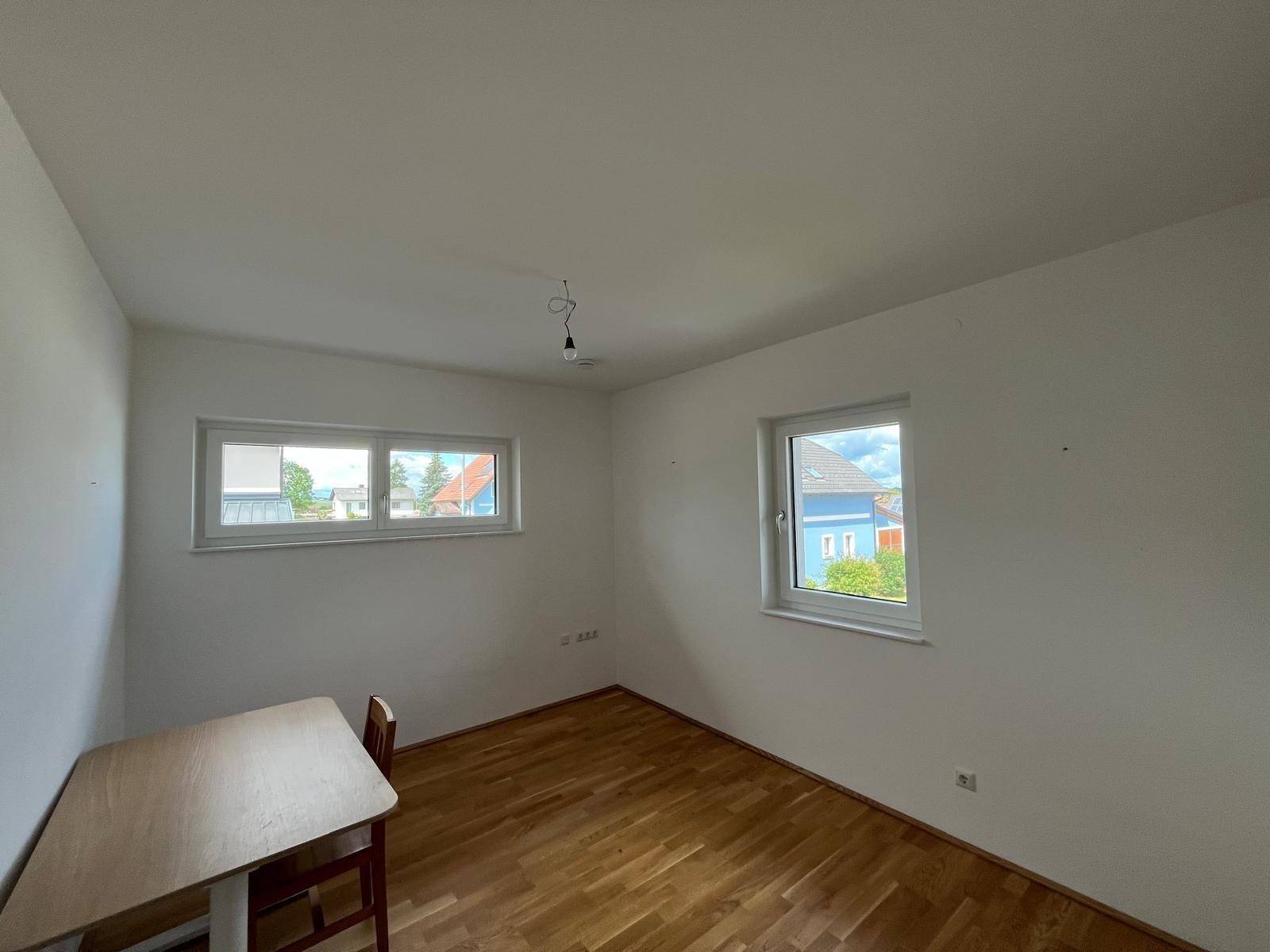 Helles Zimmer mit Holzboden und zwei Fenstern, ideal als Schlaf- oder Arbeitszimmer.