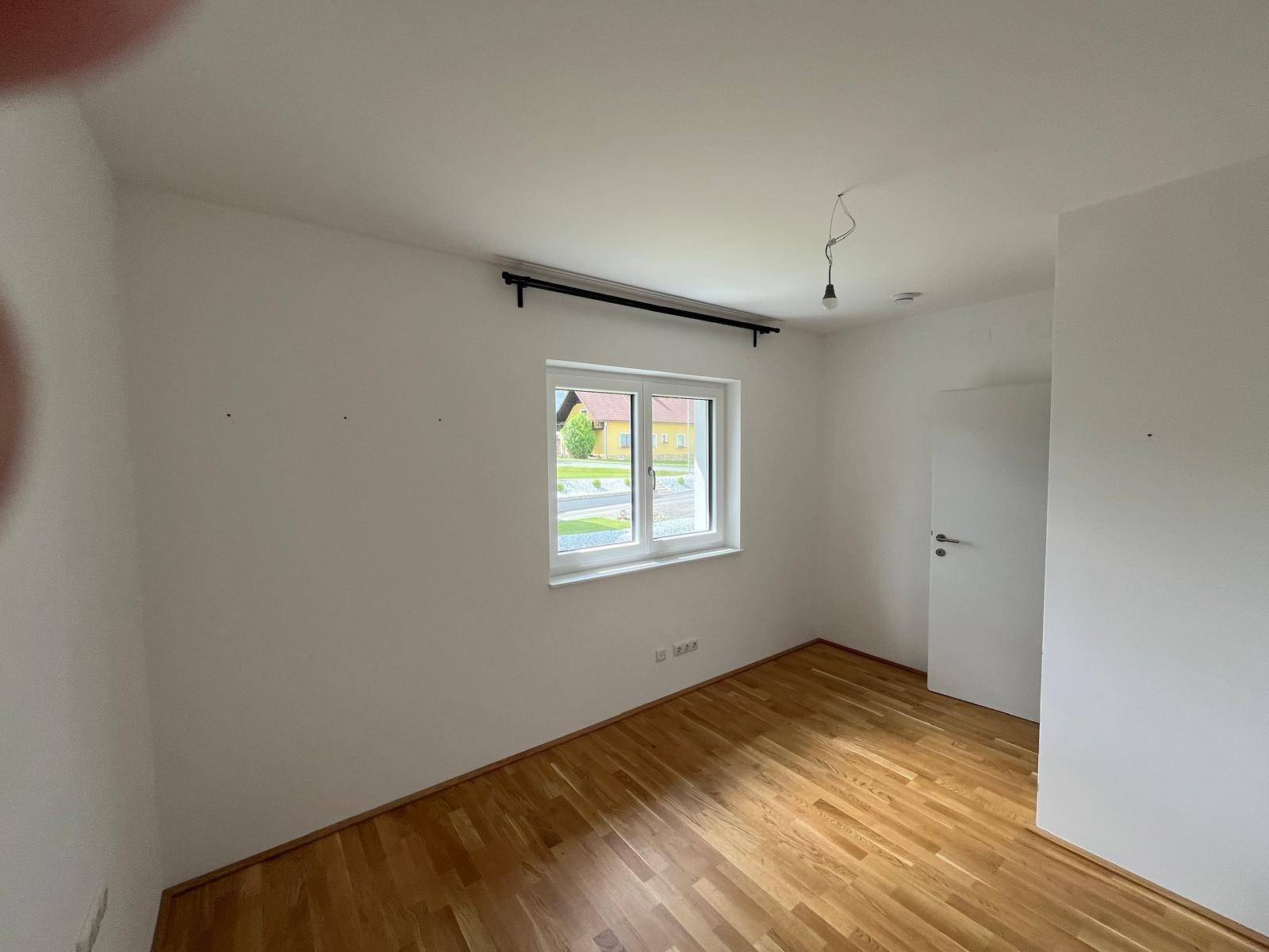 Schlafzimmer mit Holzboden, hellen Wänden und einem Fenster mit Blick ins Grüne.