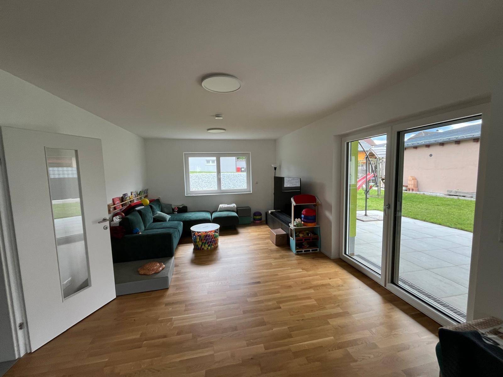 Helles Wohnzimmer mit Holzboden, großer Couch und Zugang zur Terrasse und zum Garten.