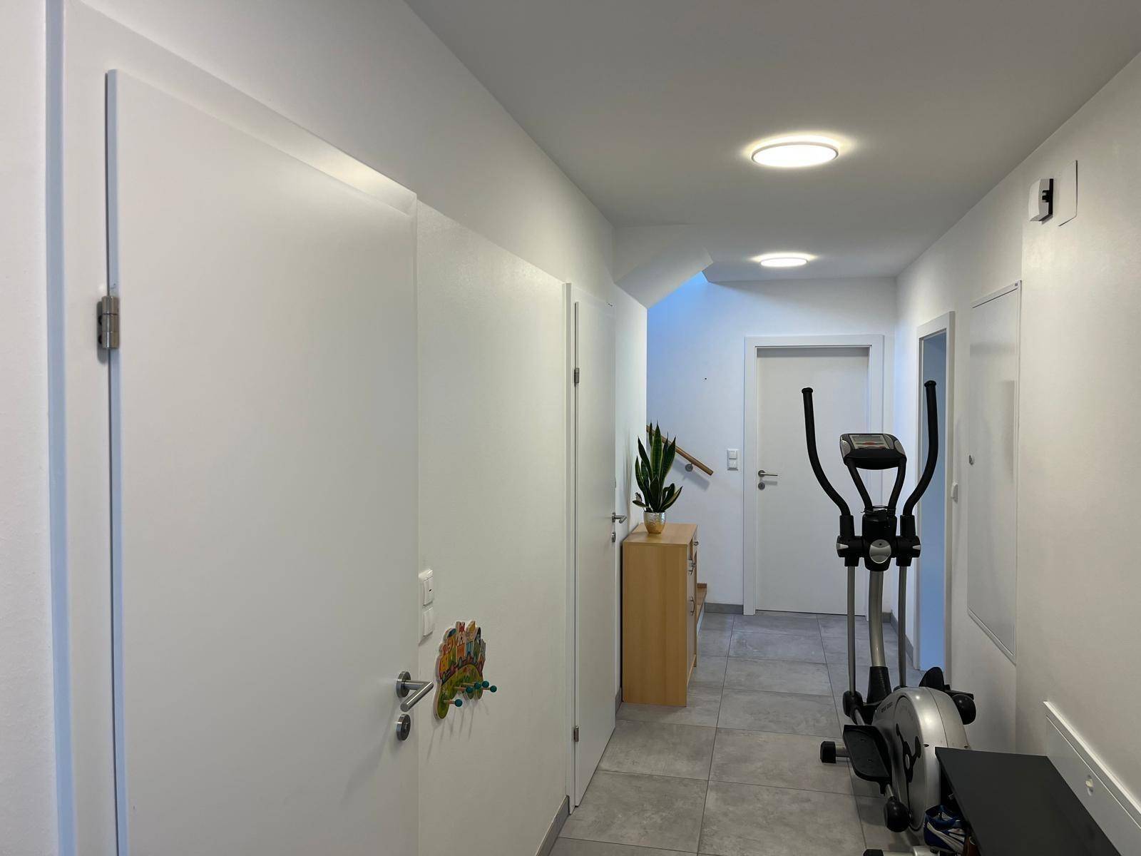 Heller Flur mit modernen Fliesen, weißen Türen und einem Fitnessgerät.