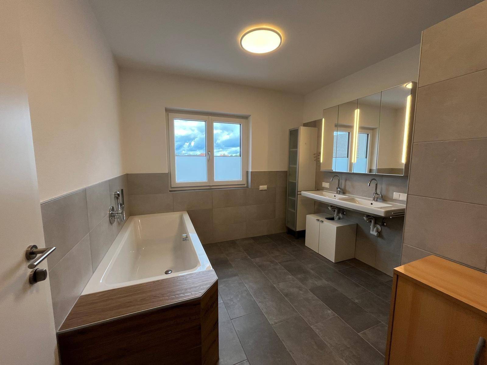 Modernes Badezimmer mit Doppelwaschbecken, Badewanne und großen Fliesen.