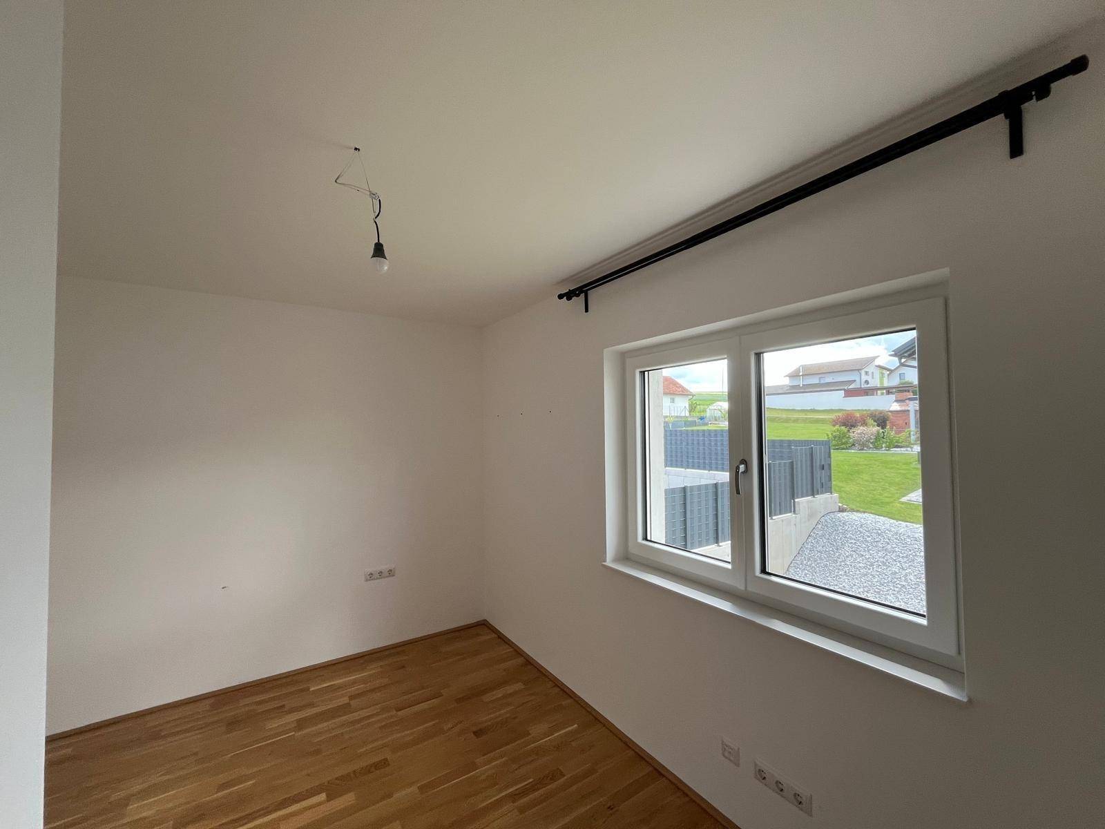 Helles Zimmer mit Holzboden und großem Fenster mit Blick auf den Garten.