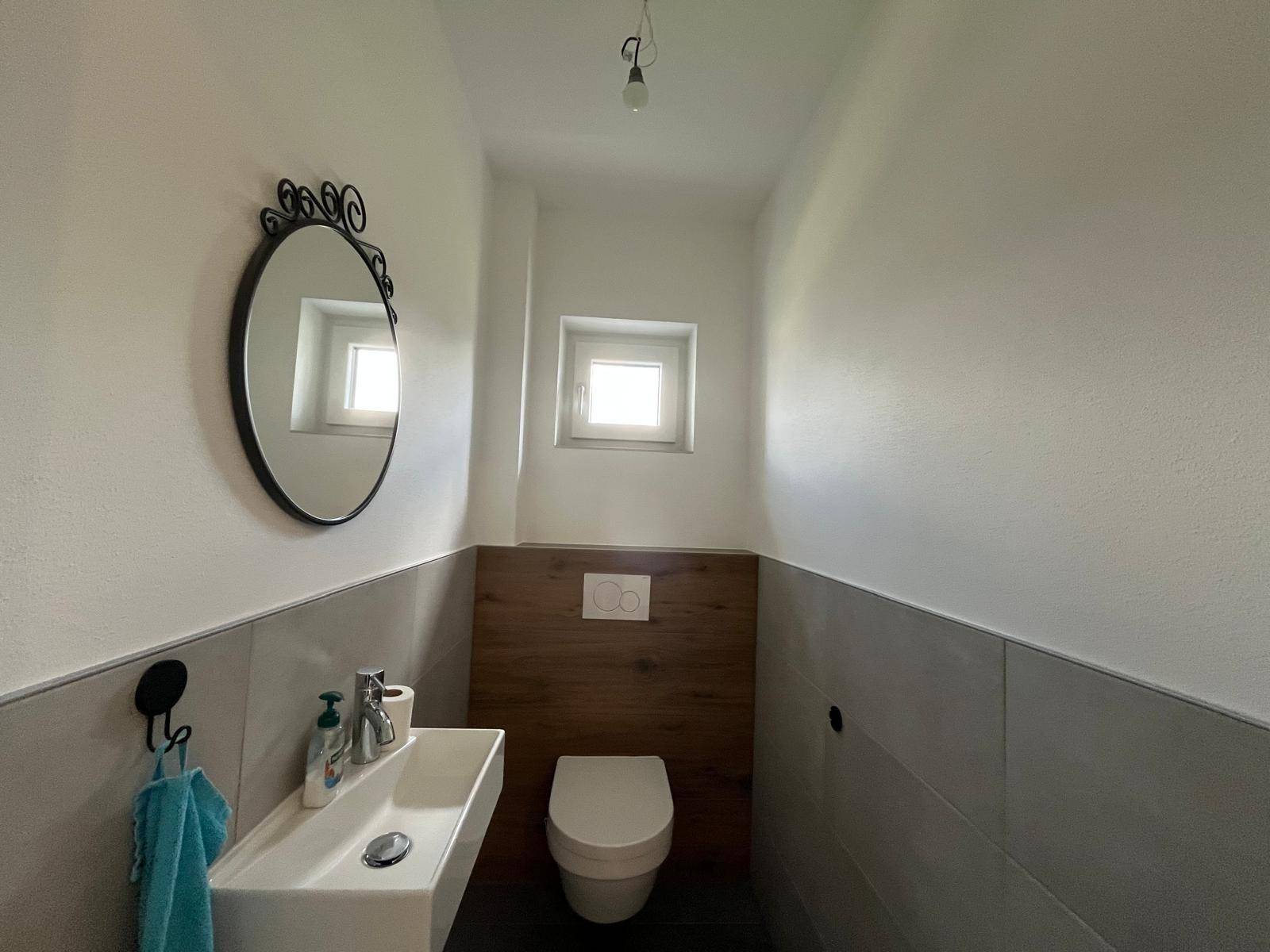 Modernes Gäste-WC mit wandhängendem WC, kleinem Waschbecken und Fenster.
