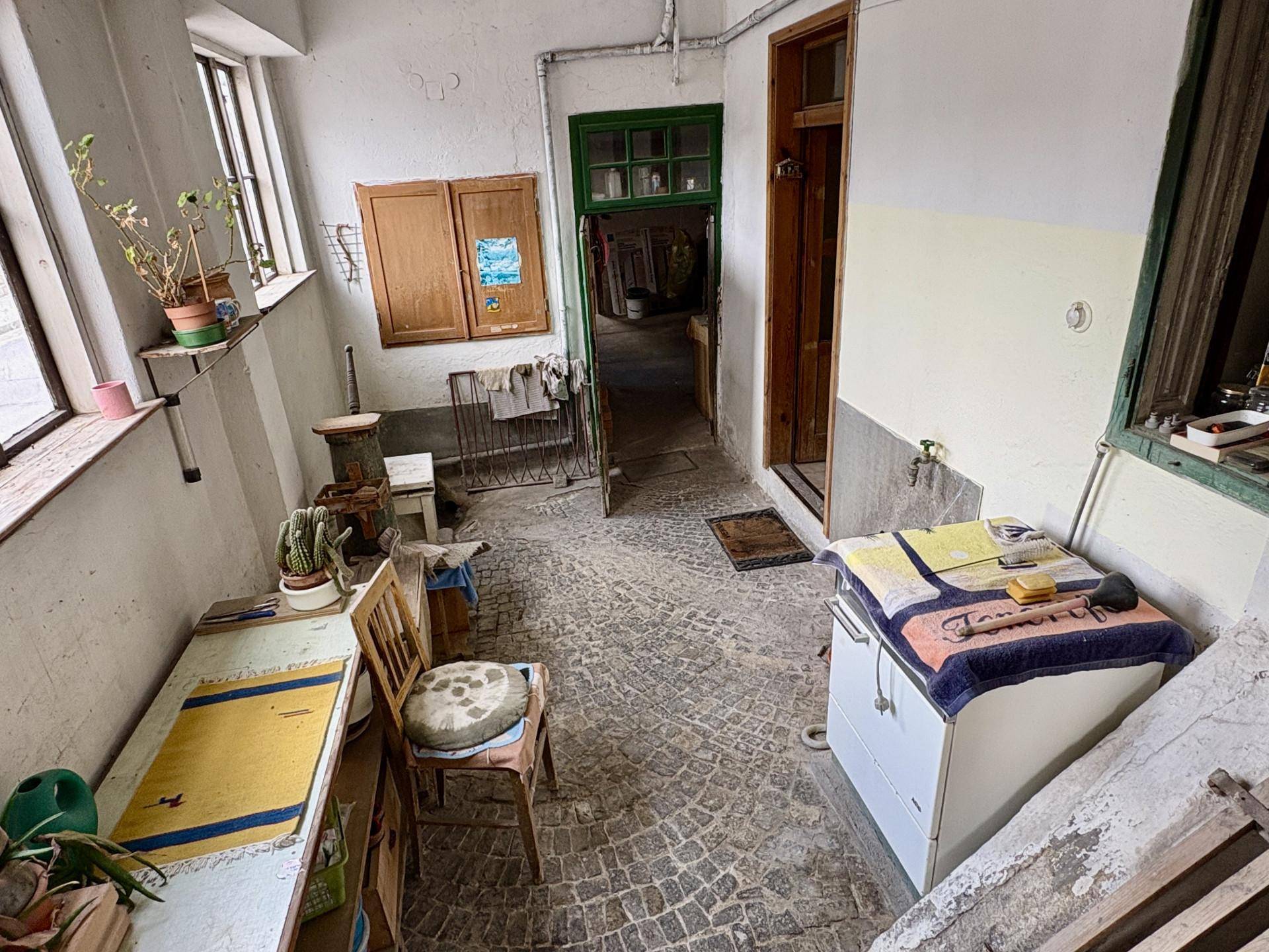Rustikaler Hauswirtschaftsraum mit Kopfsteinpflasterboden, alten Möbeln und Fenstern, die viel Licht hereinlassen.