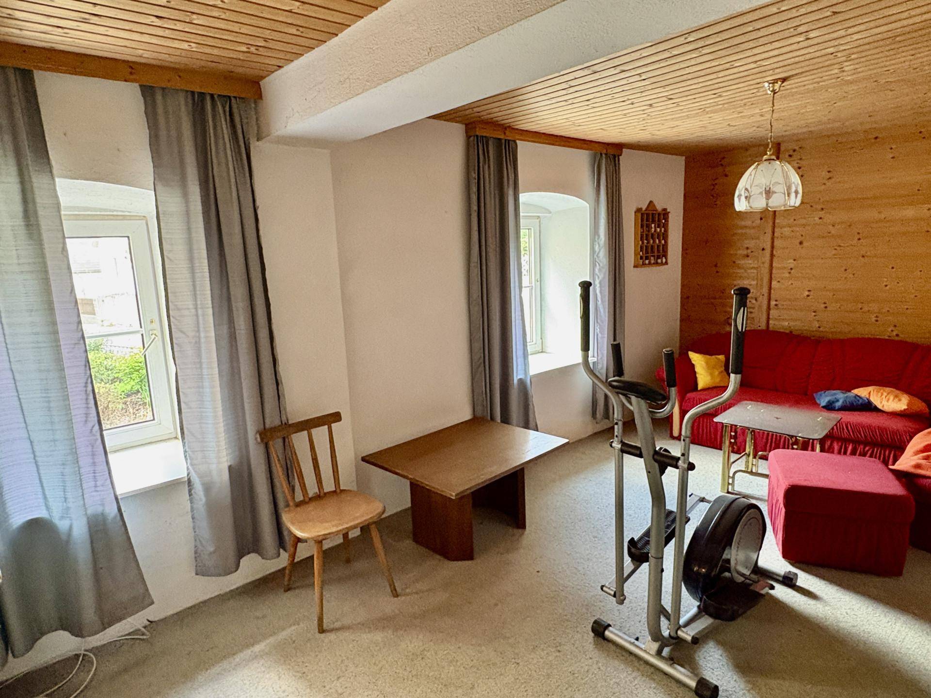 Gemütliches Wohnzimmer mit Holzvertäfelung, rotem Sofa und einem Fitnessgerät, ideal für Sport und Entspannung.